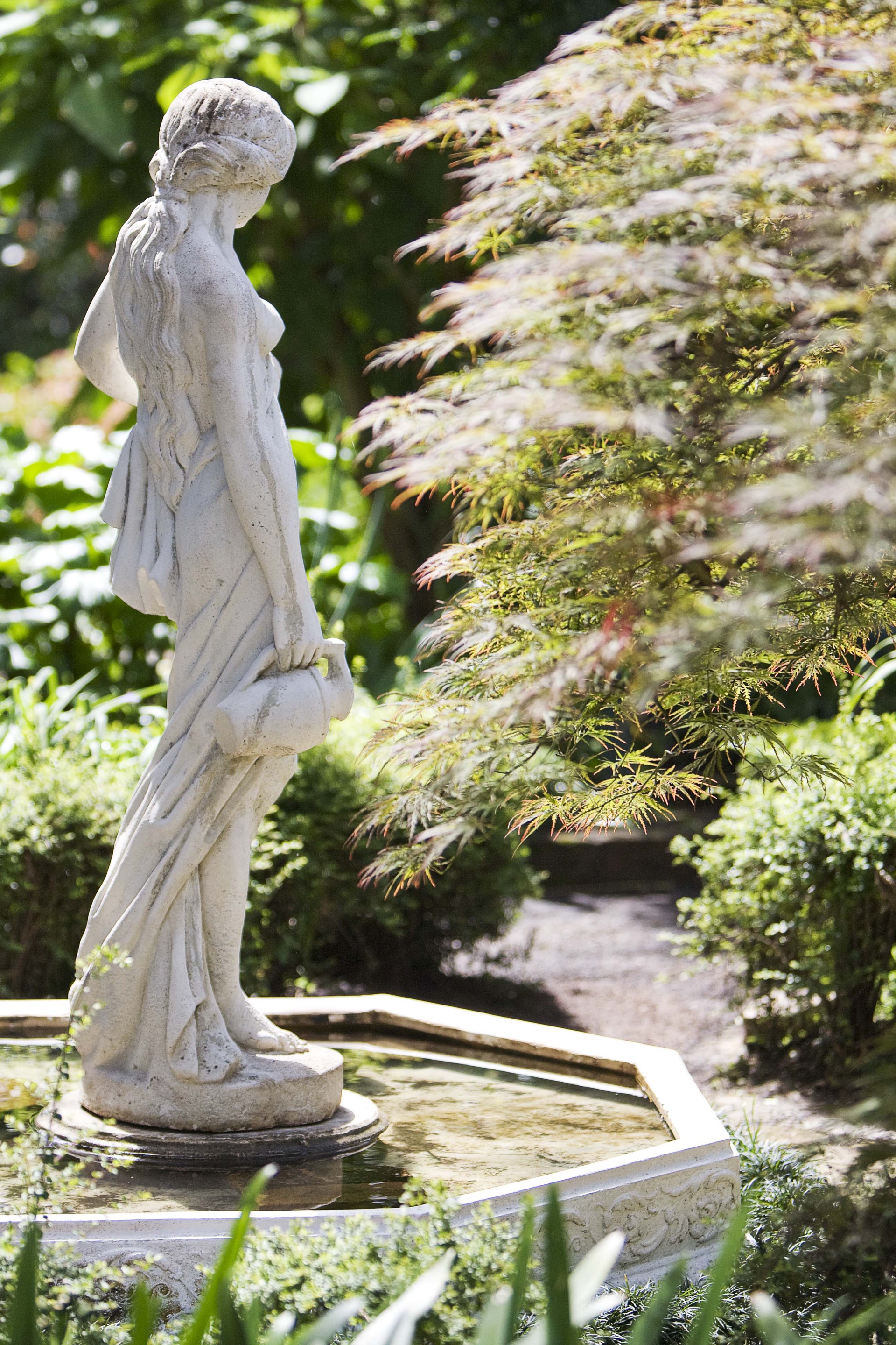 Garden statue in the foreground with a Japanese maple tree in the background.
