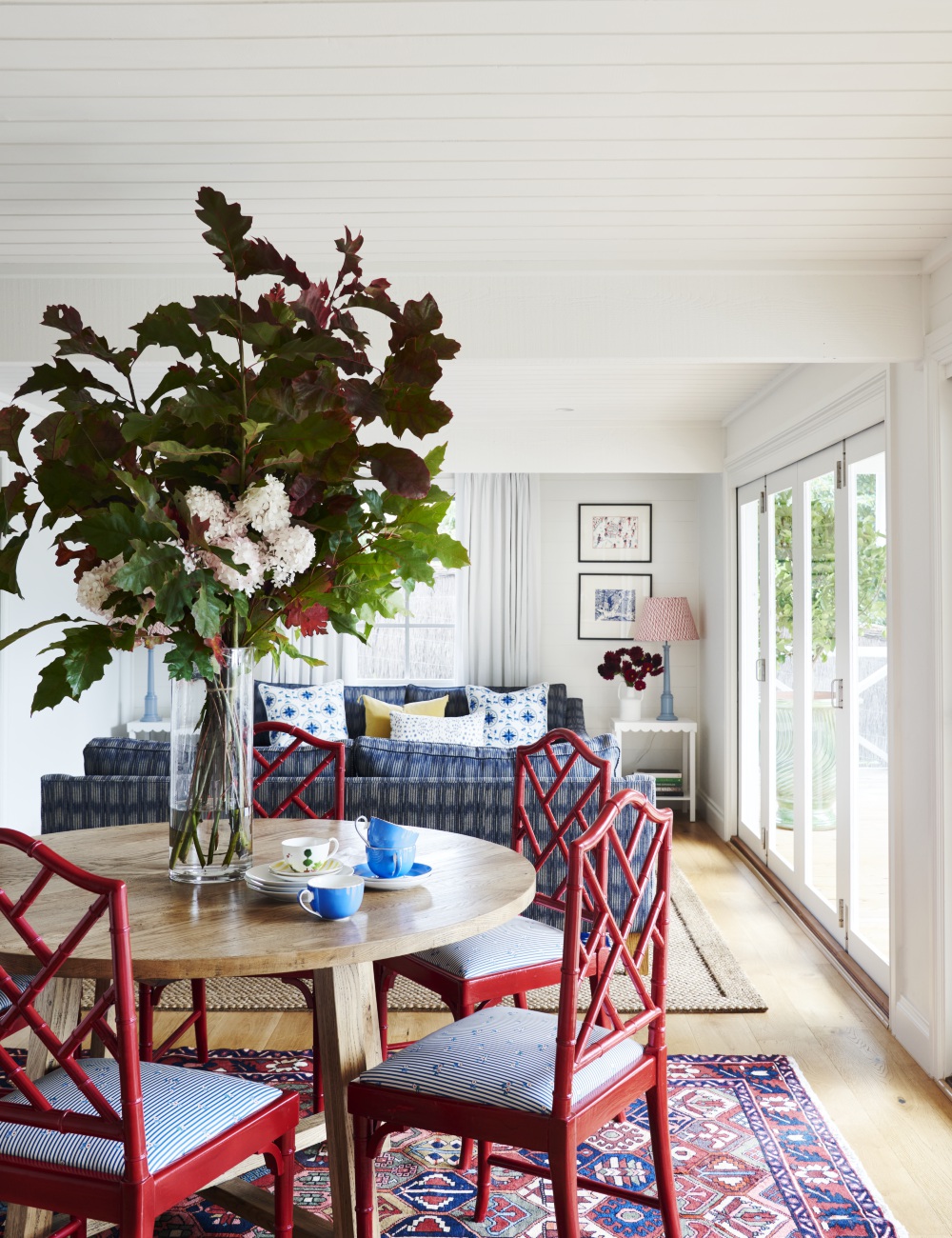 Open plan living dining room with round table and red painted upholstered dining chairs