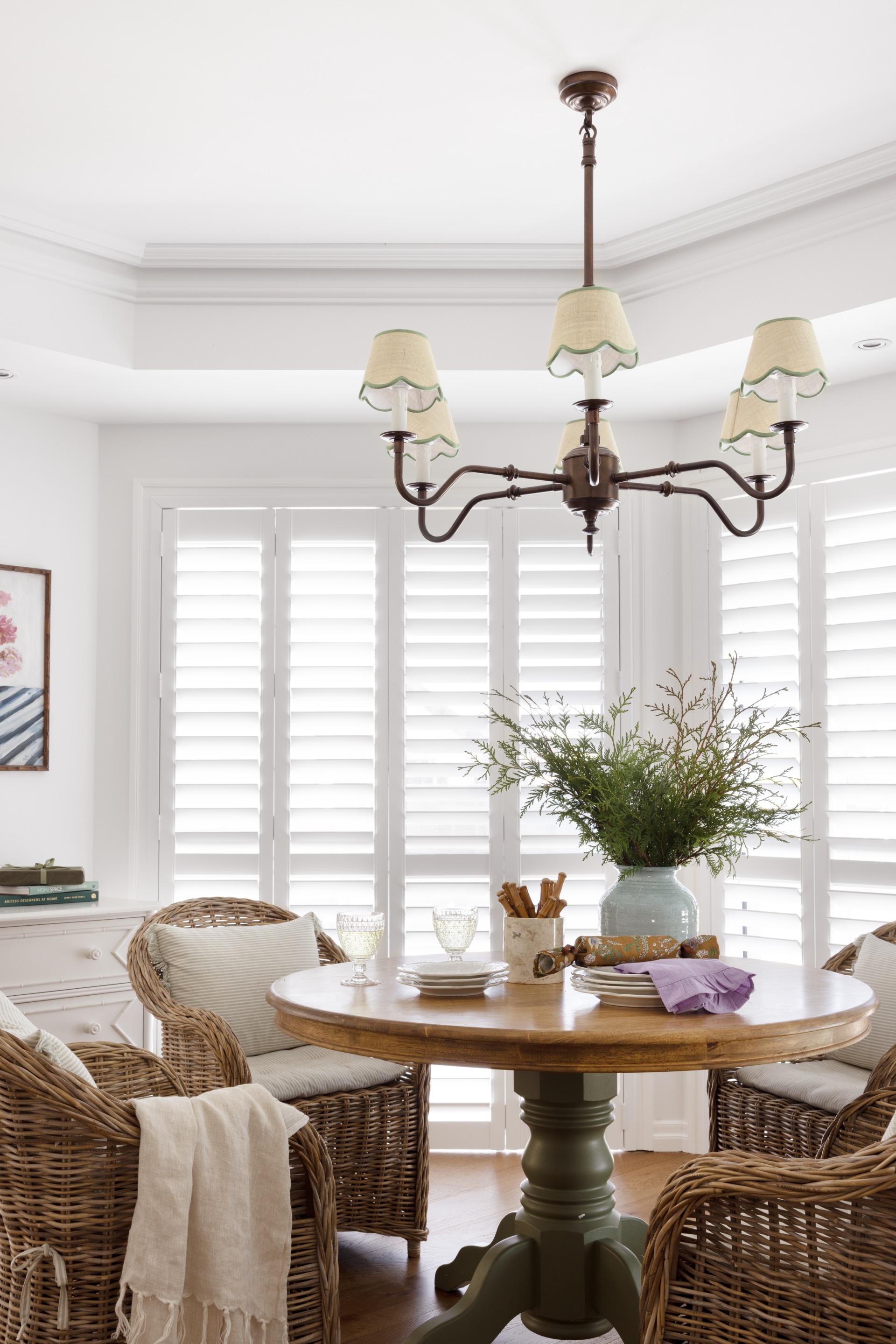 A sitting area in bright white with rattan armchairs and a classic round timber table.