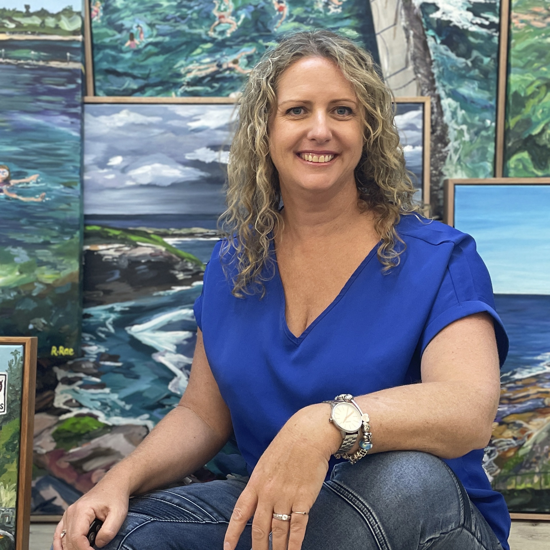 Australian artist Rachel Rae sitting by a collection of ocean artworks.