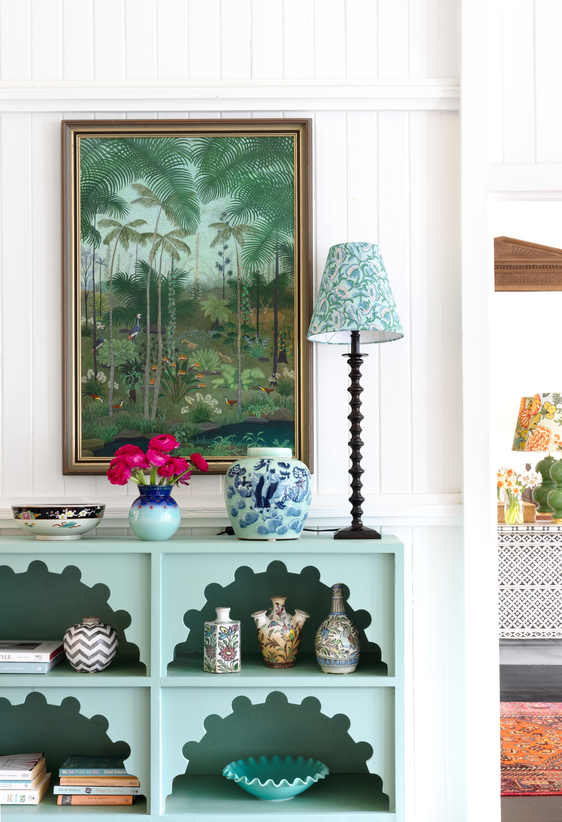 A blue antique Moroccan shelf with a tropical artwork hanging above.