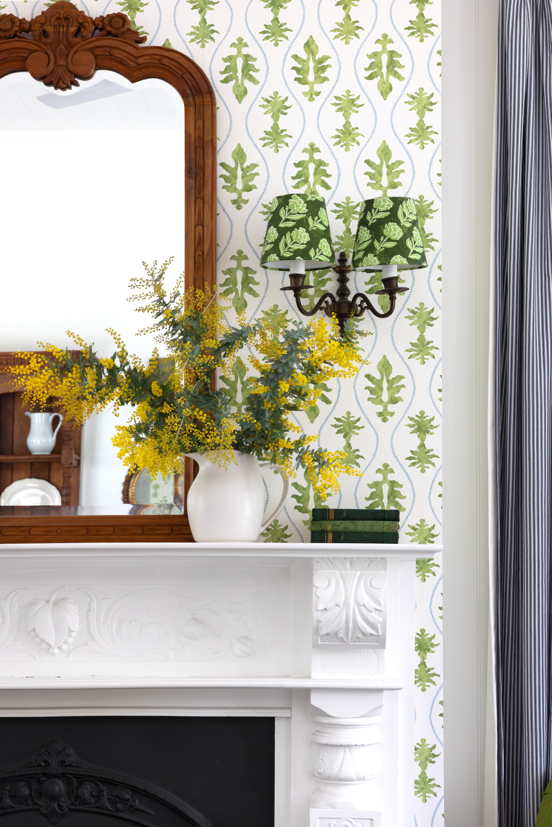 A white antique fireplace in the living area surrounded by green patterned wallpaper.