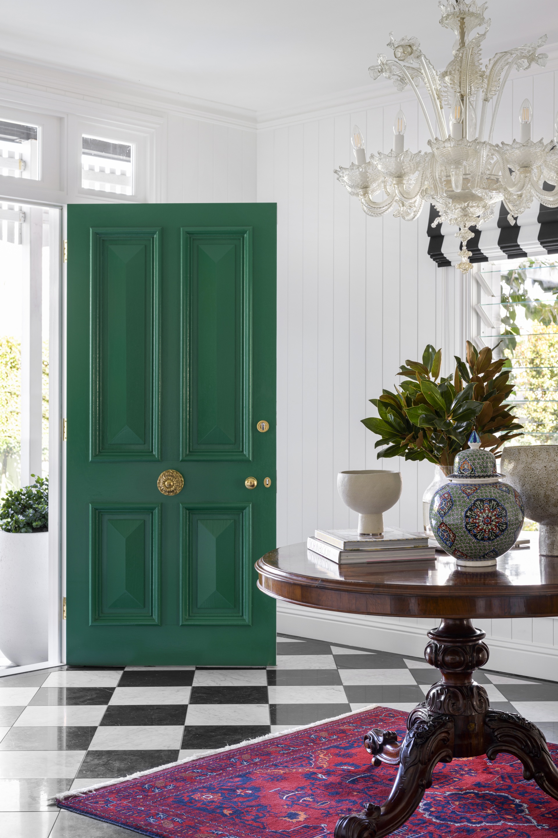A foyer with a checked floor, green door and a vintage chandelier.