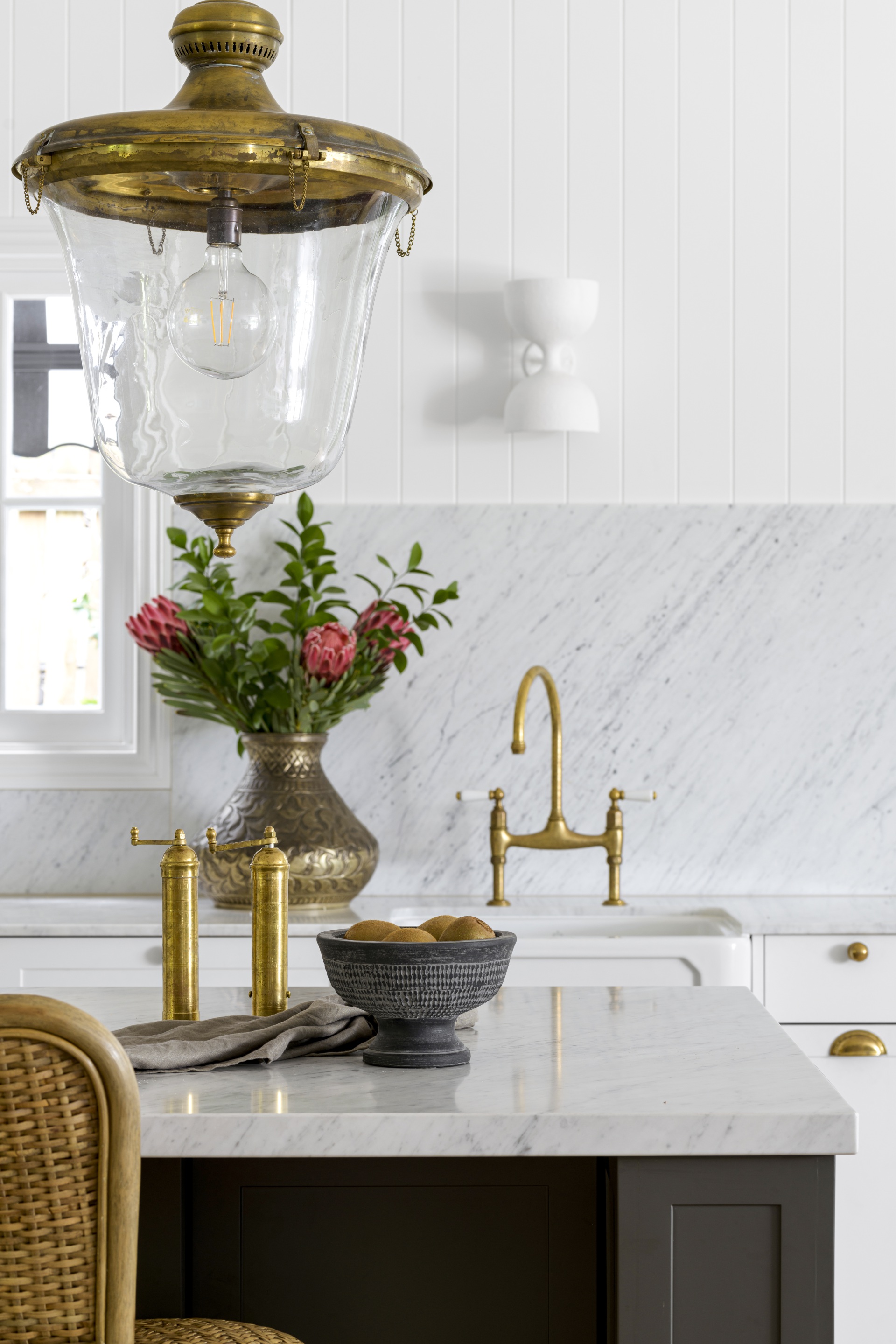 A white French style kitchen with a gold antique hanging light.