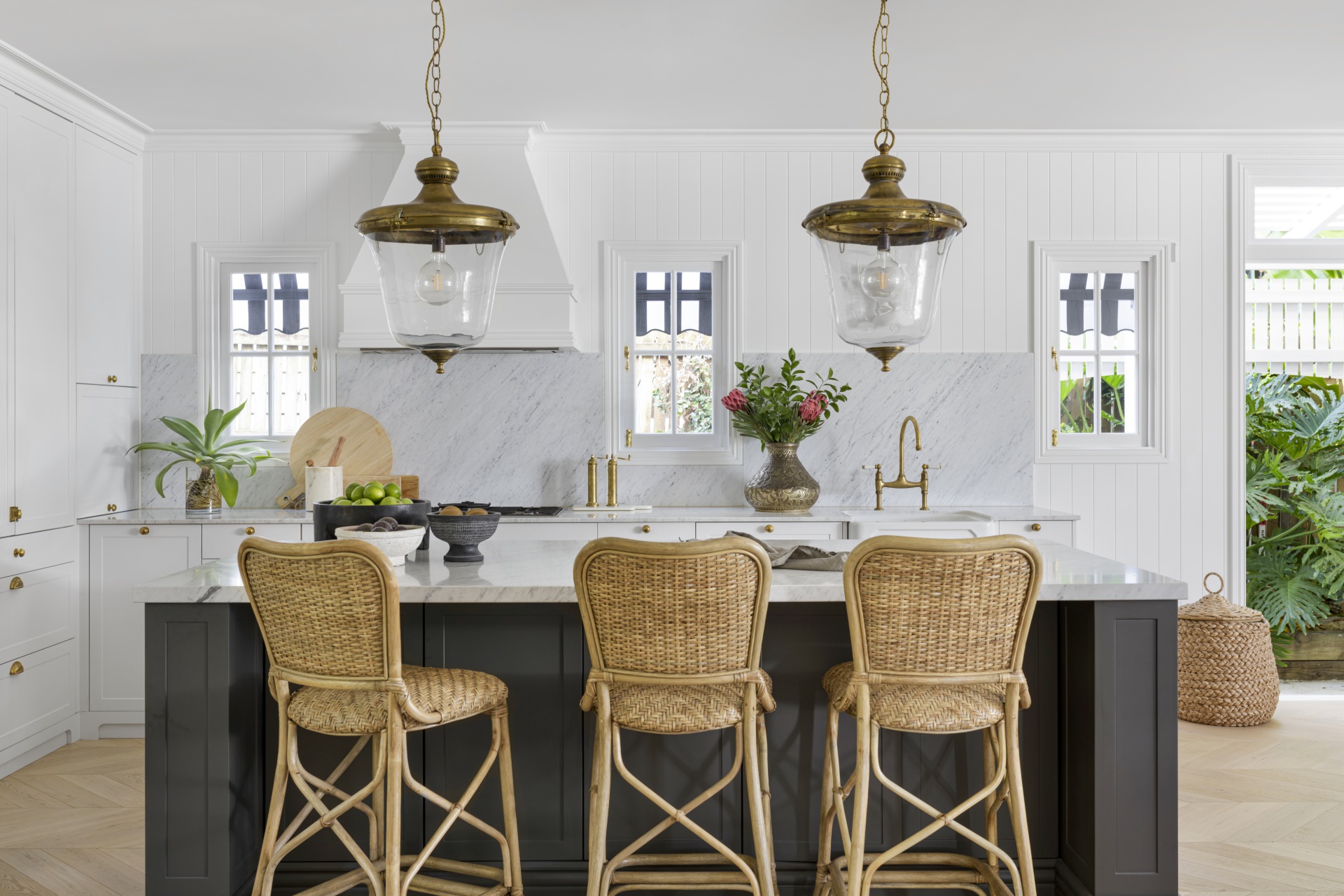 A white and marble French-inspired kitchen with an island and rattan chairs.