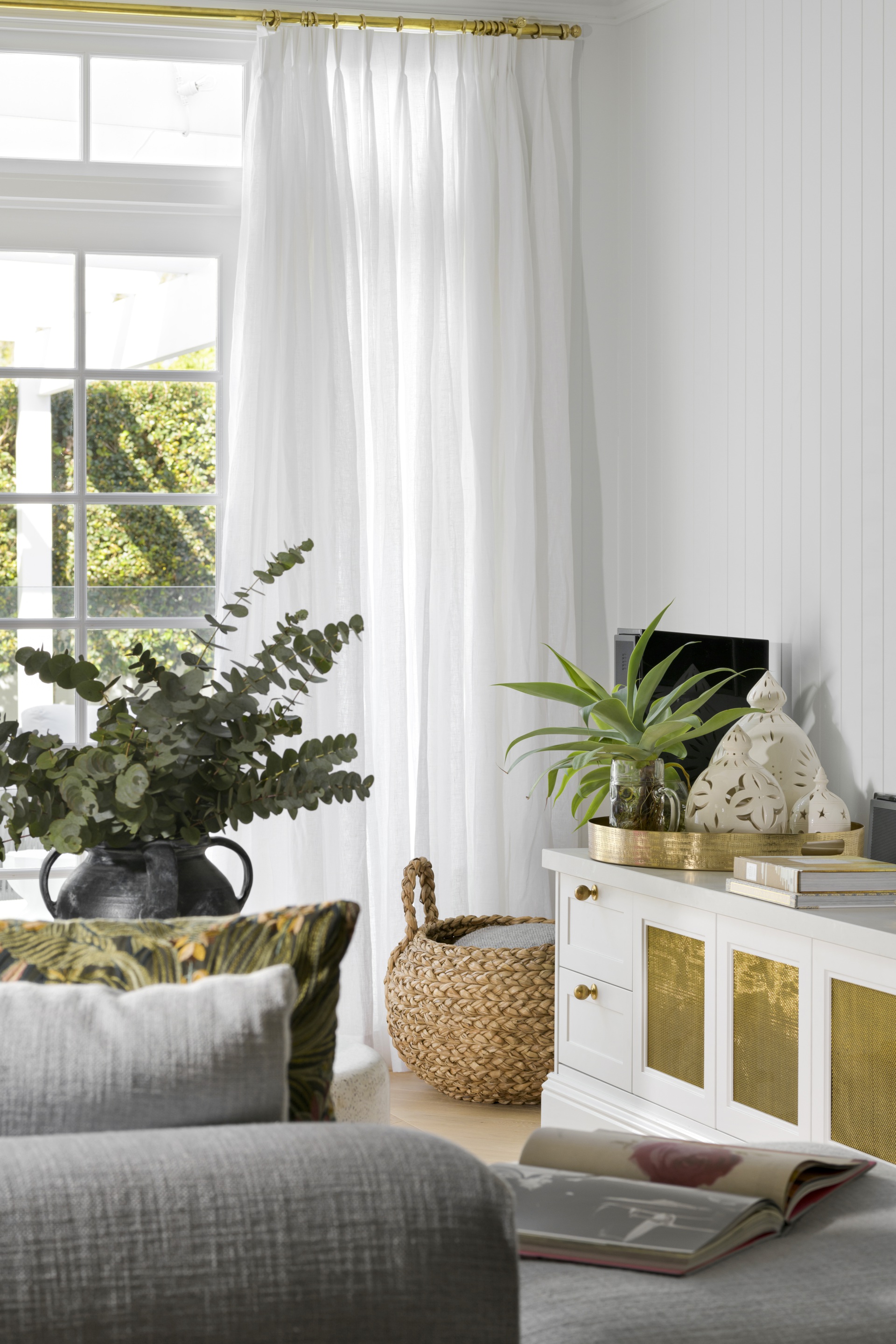 French windows with white curtains by a sideboard and rattan basket.