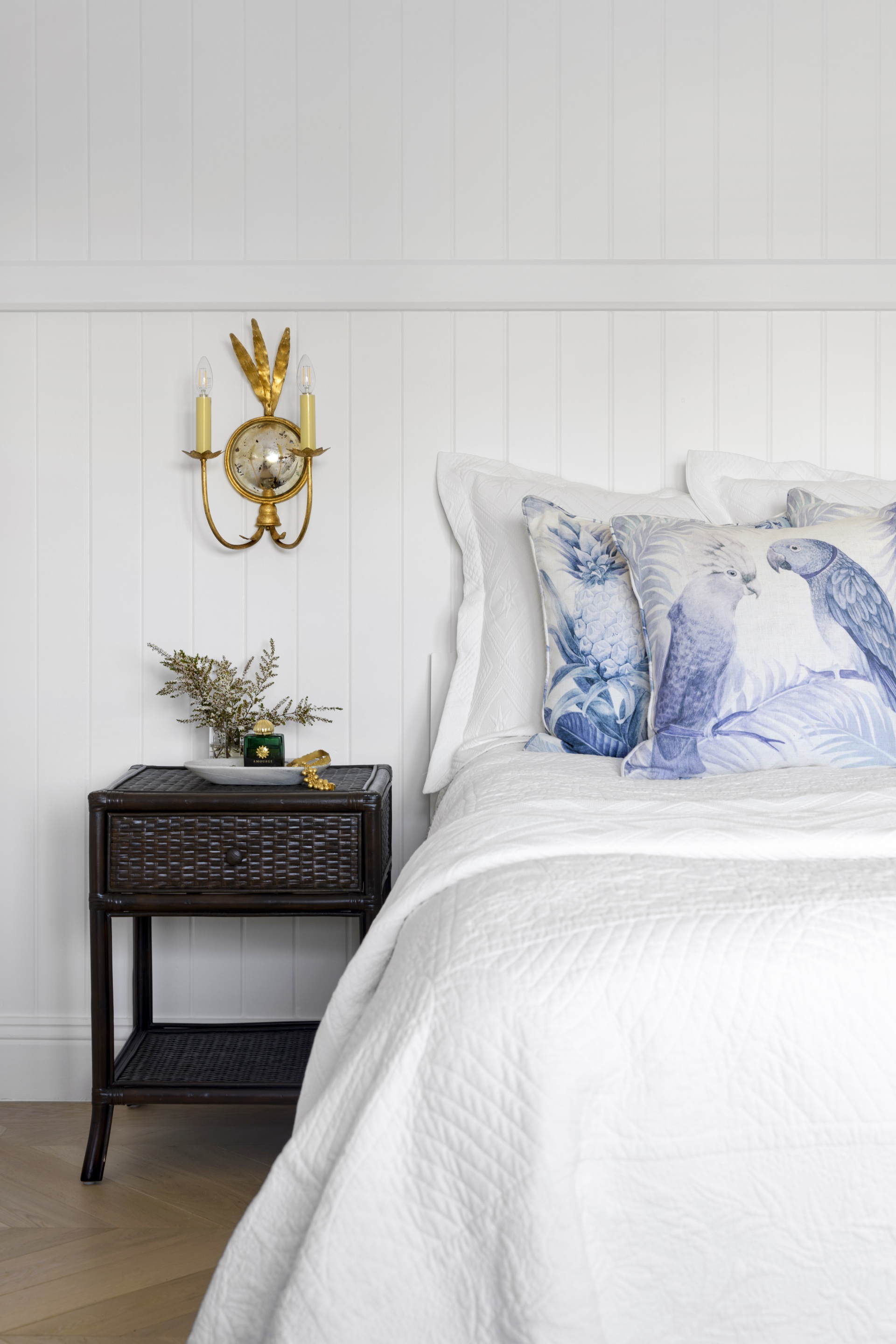A contemporary white bedroom with a black rattan bedside table.