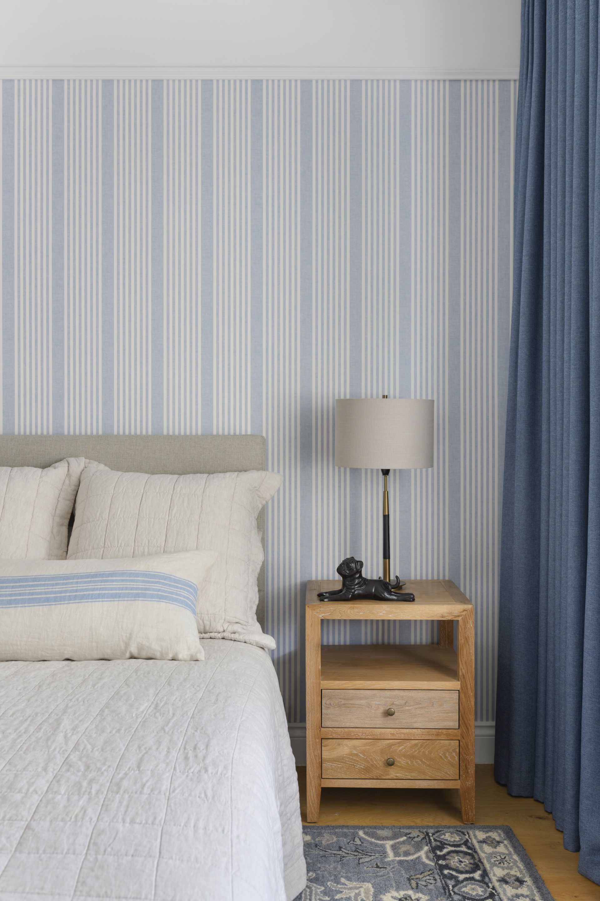 A children's bedroom with blue striped wallpaper and grey bed.