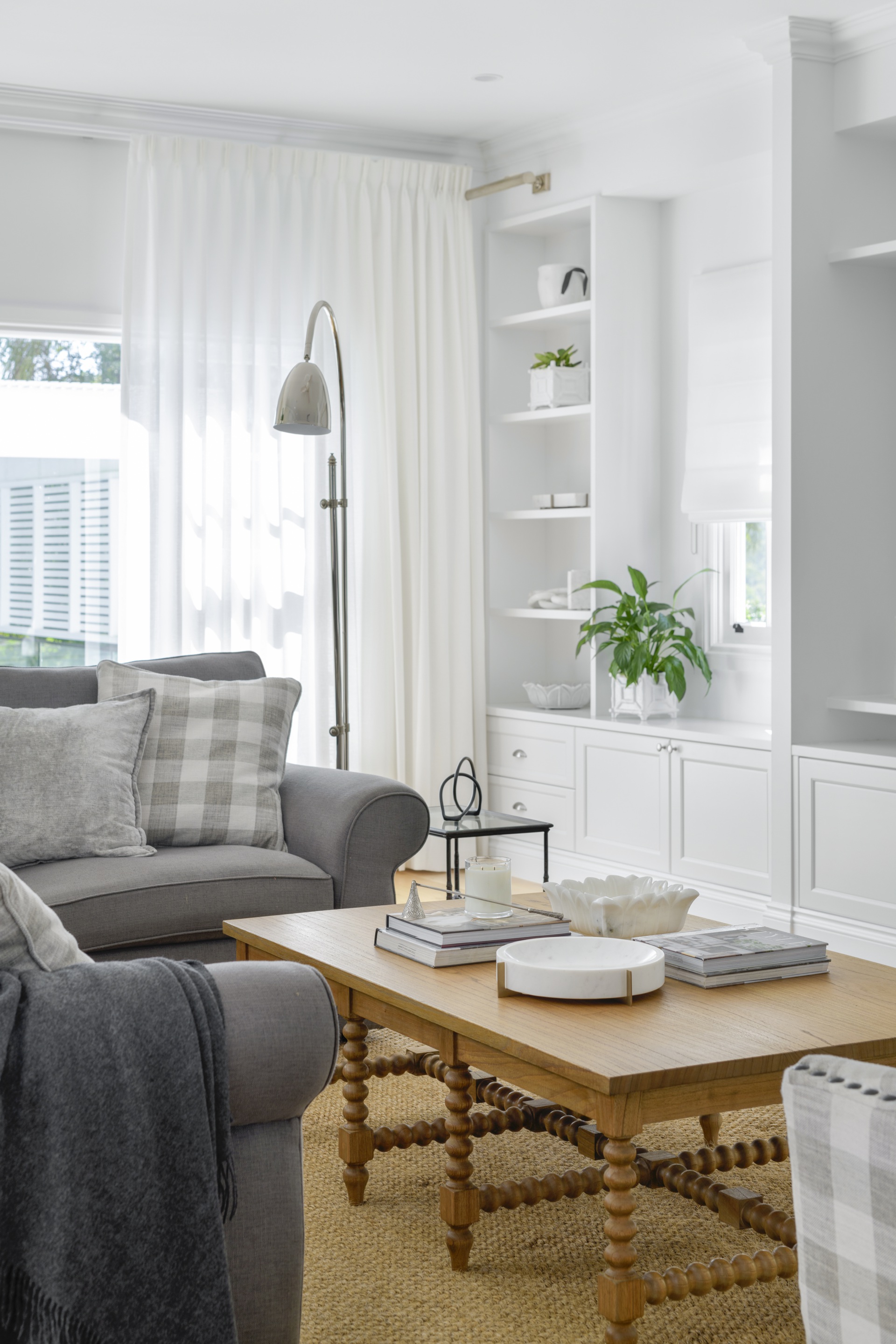 A white living room with a timber coffee table, grey sofas and open shelving.
