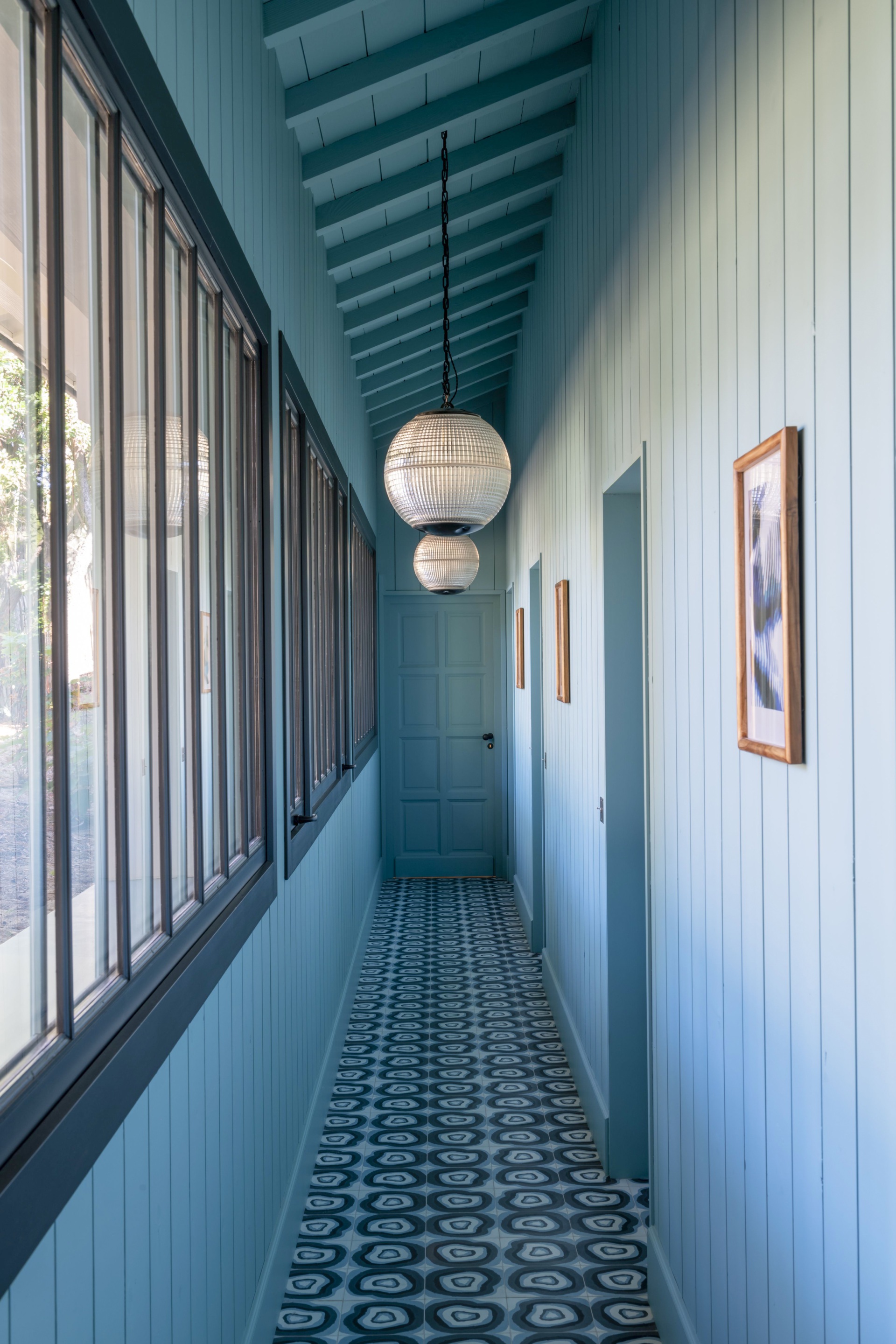 A blue hallway with patterned floor tiles and hanging globe pendants.