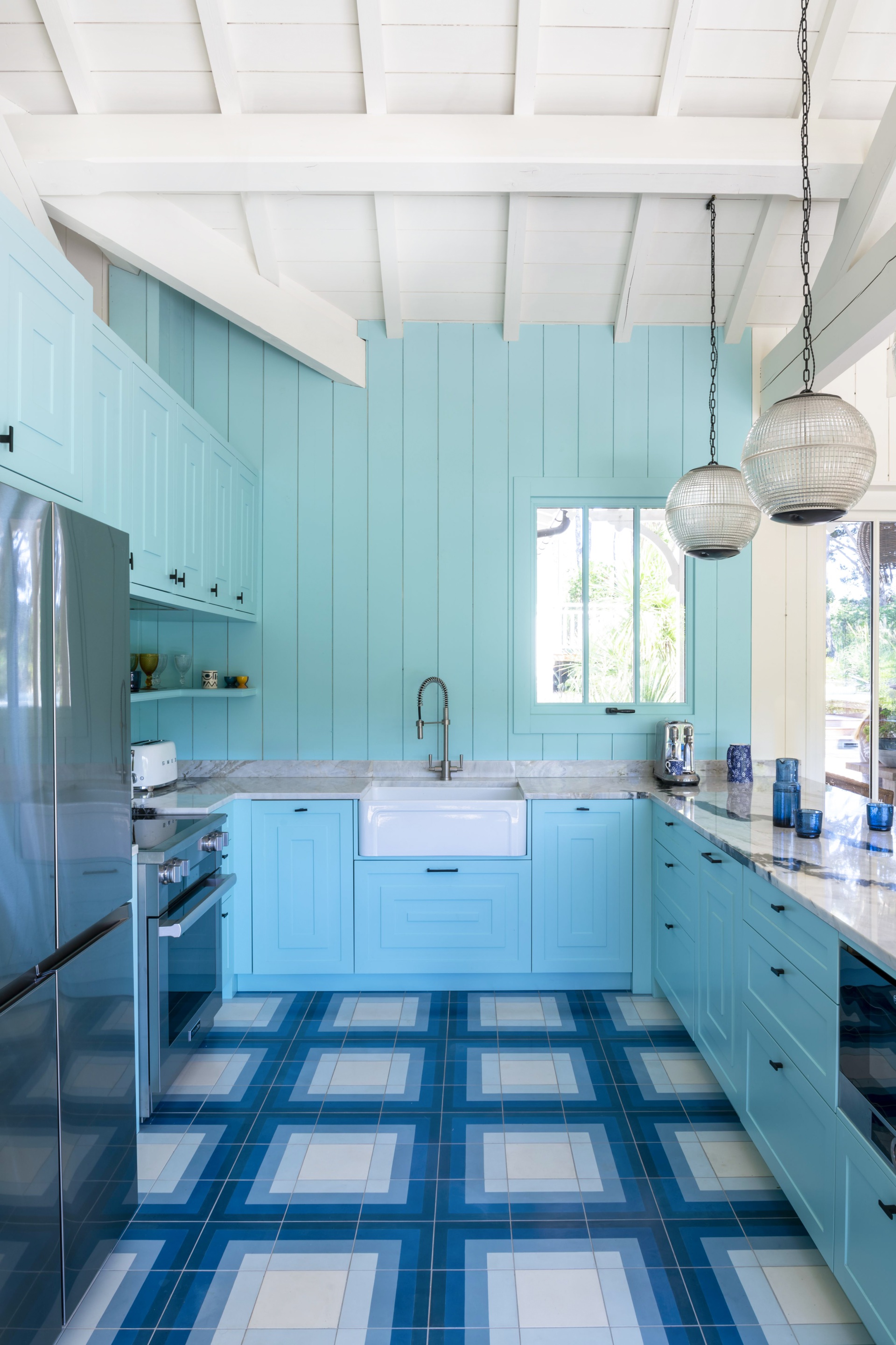 A coastal kitchen with blue wall panels, a butler's sink and geometric floor tiles.
