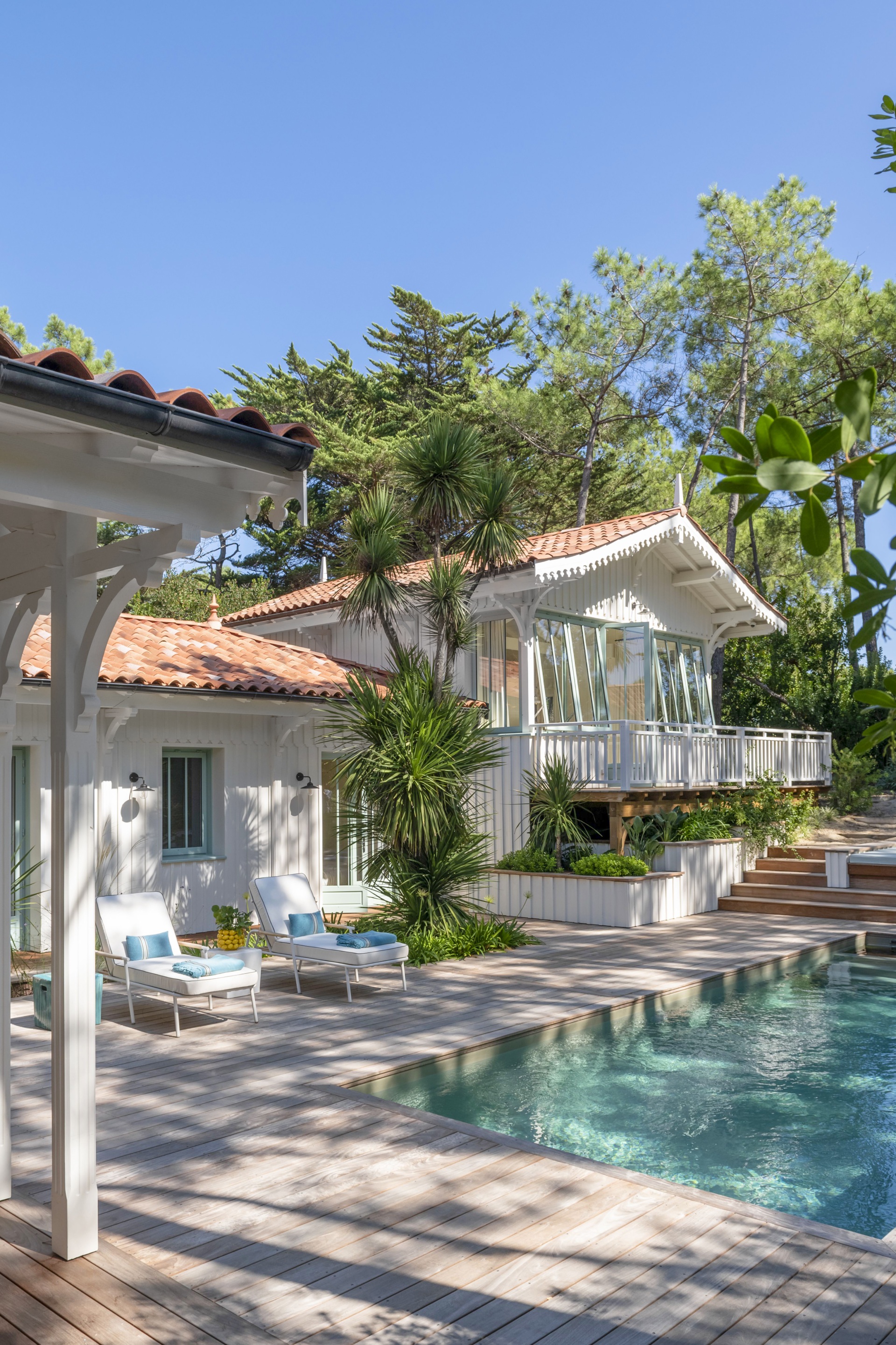 A pool and deck area with tropical plants by a white fenced balcony.