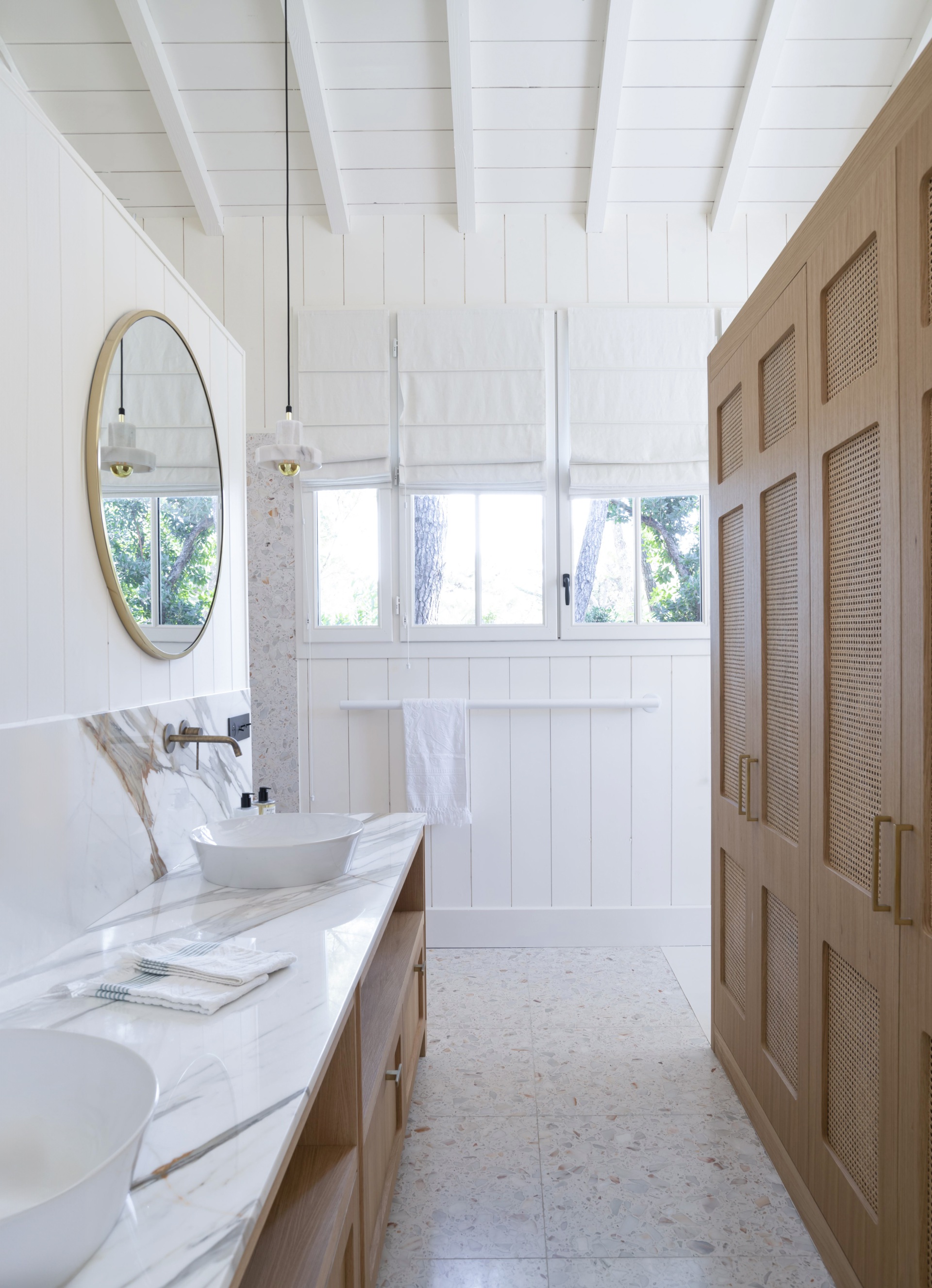 A white coastal bathroom with a marble vanity and timber wicker cabinets.