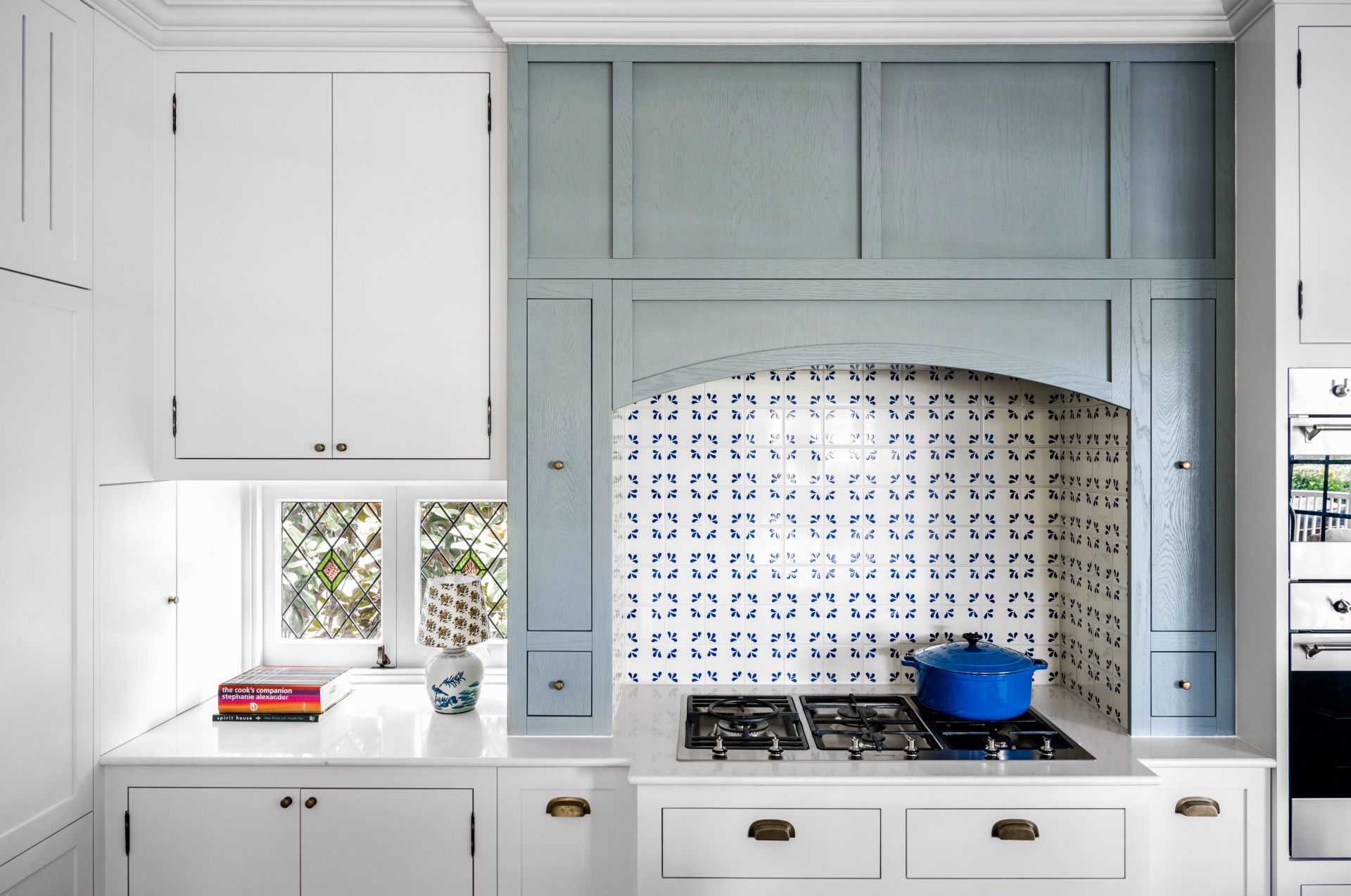 A cottage kitchen with a mosaic splashback, stove top and blue timber joinery.
