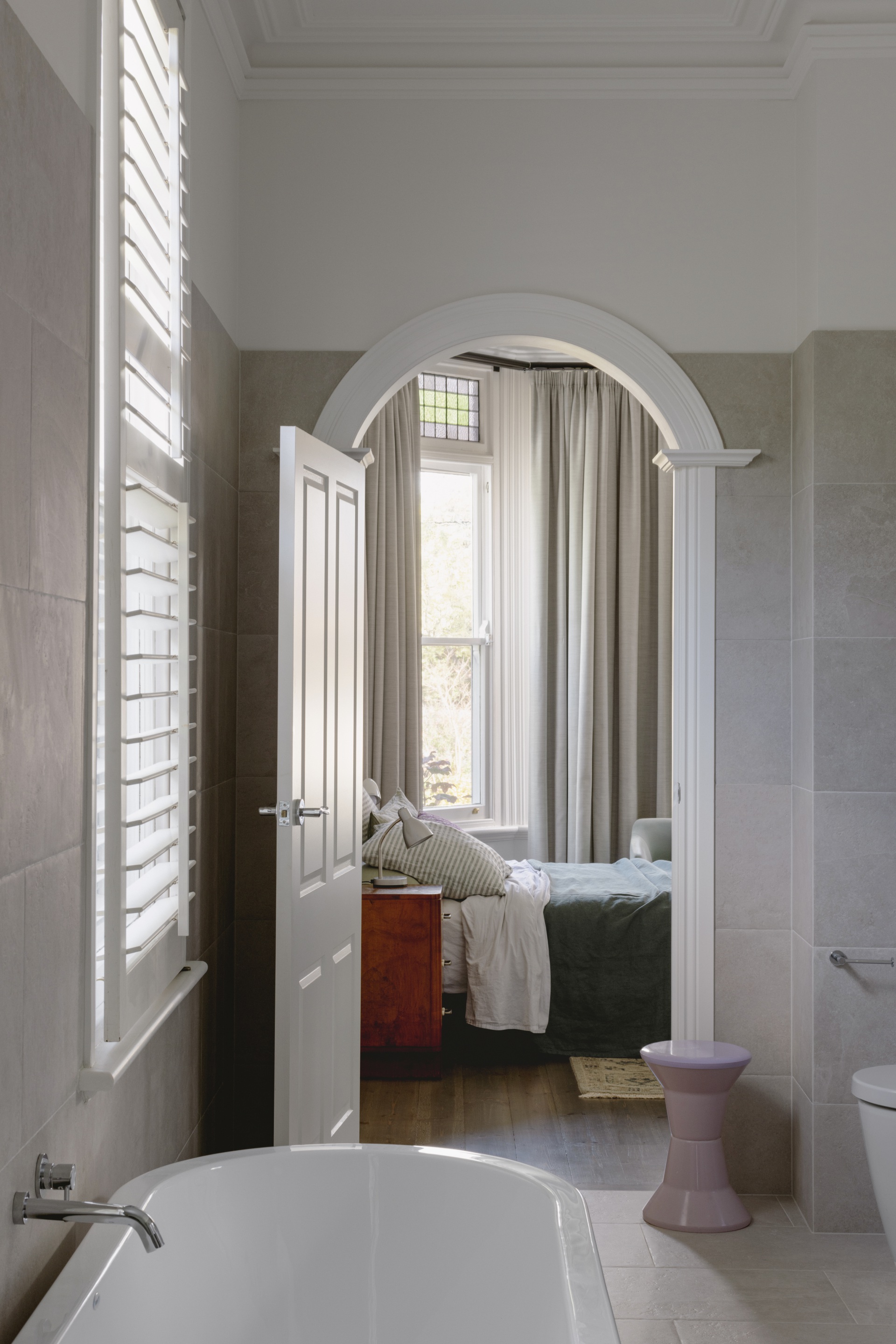 A main ensuite with large-scale neutral tiles and an archway into the bedroom.