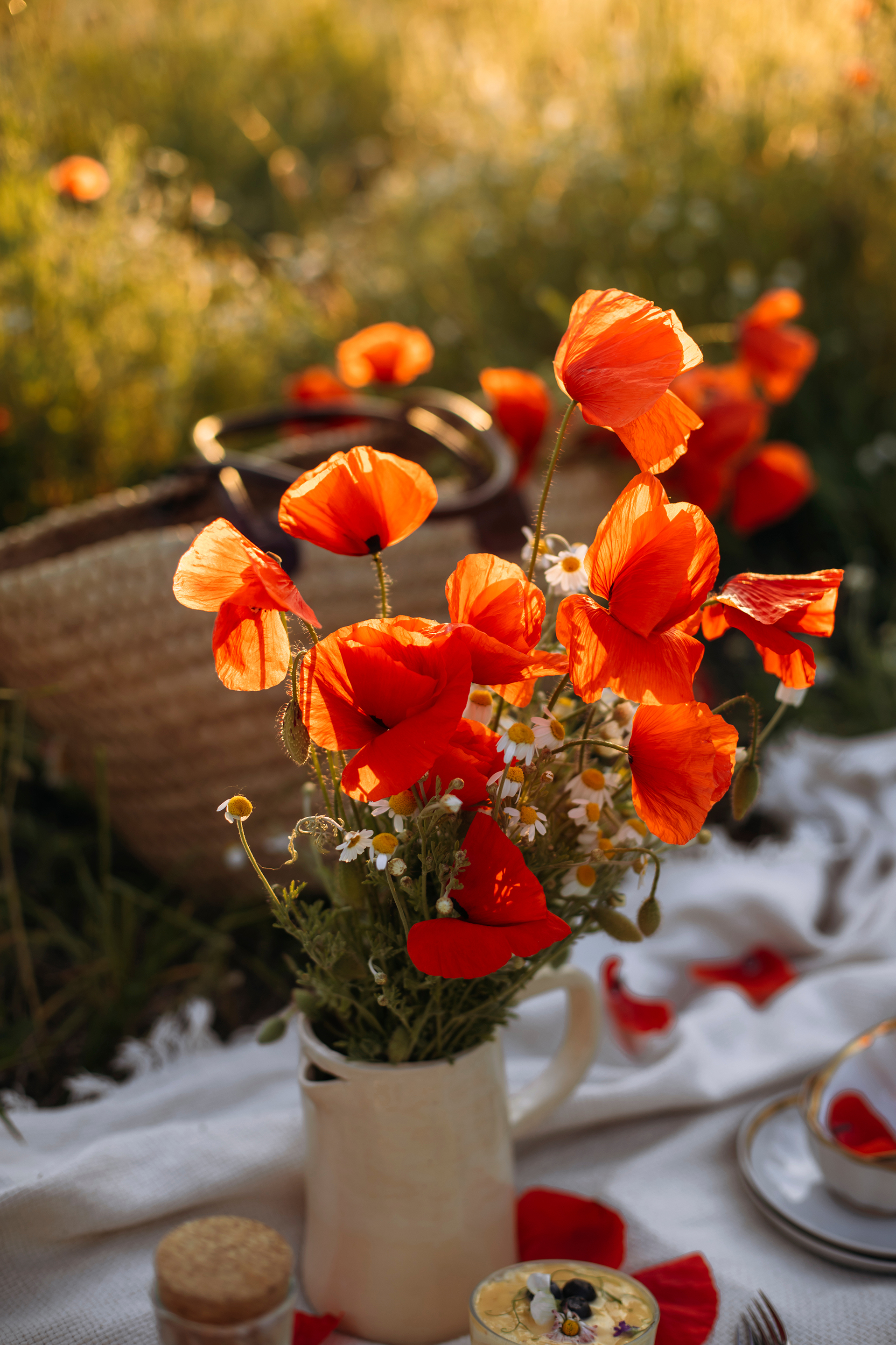 Red poppies and camomile flowers in a vase on an outdoor dining table.
