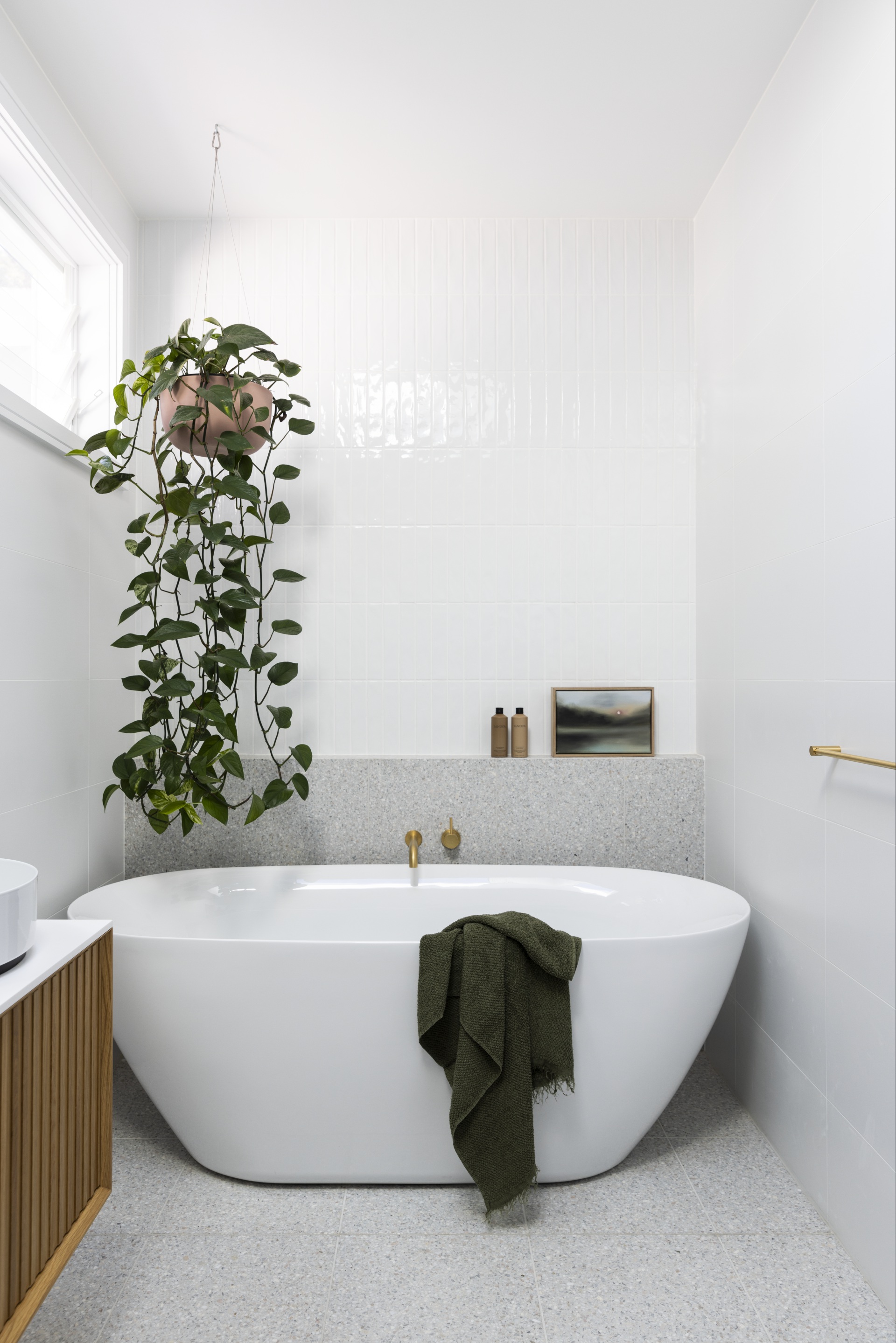 A white and grey tiled bathroom with a freestanding bath and hanging plant.