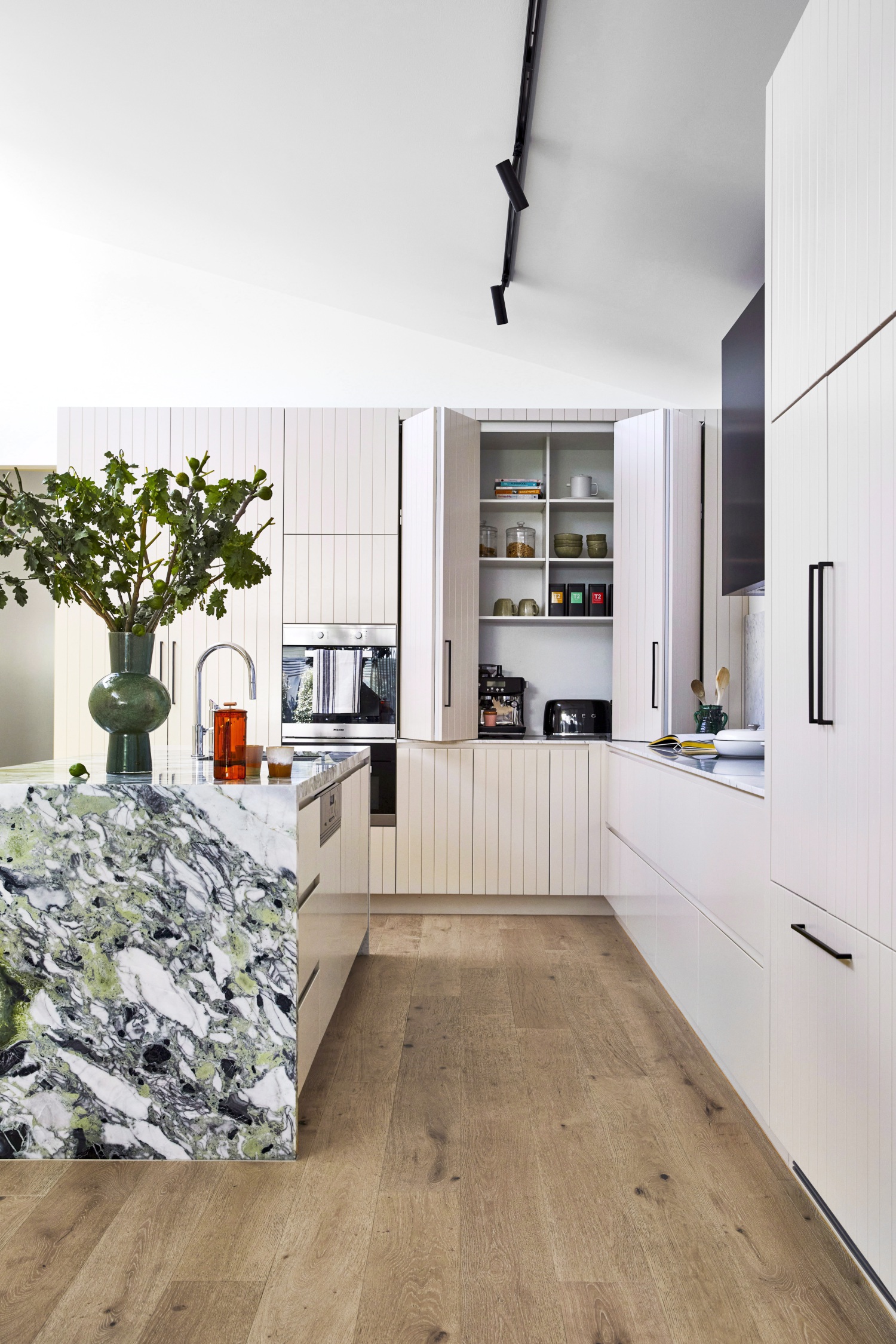 A kitchen with a marble island and white panelled retractable cupboard doors.