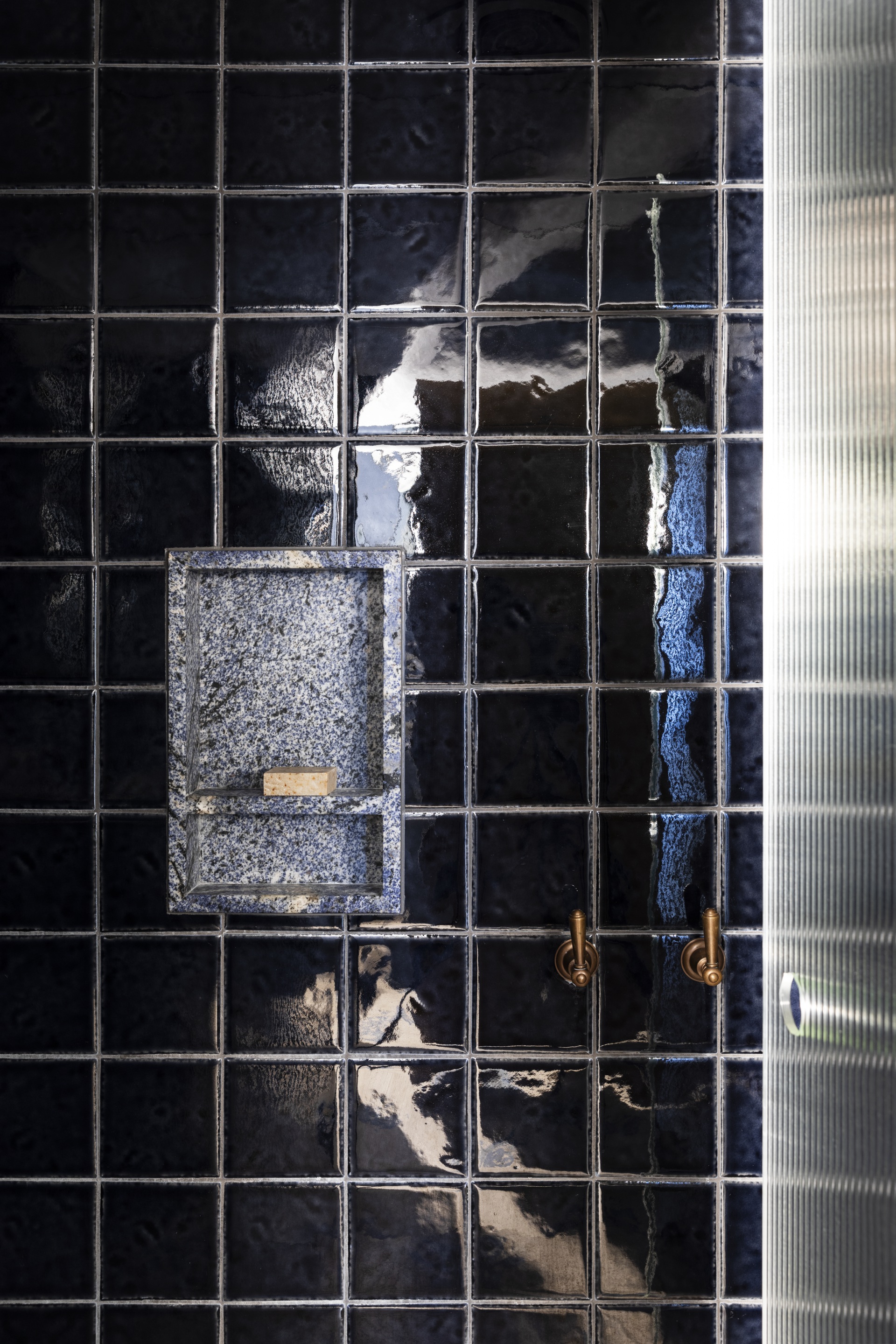 A black-tiled shower with bronze tapware by a shower niche.