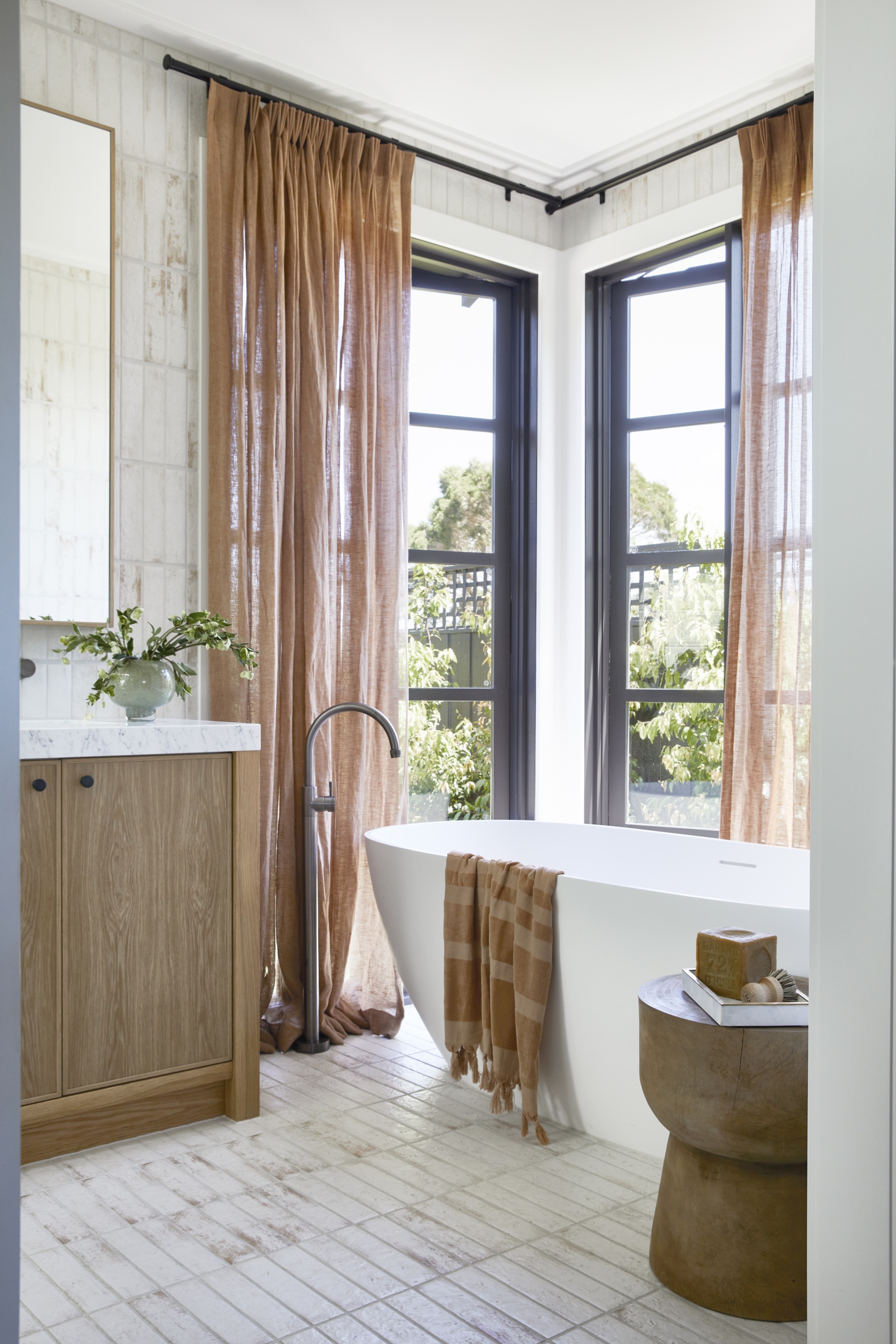 A freestanding bath surrounded by windows and blush curtains.