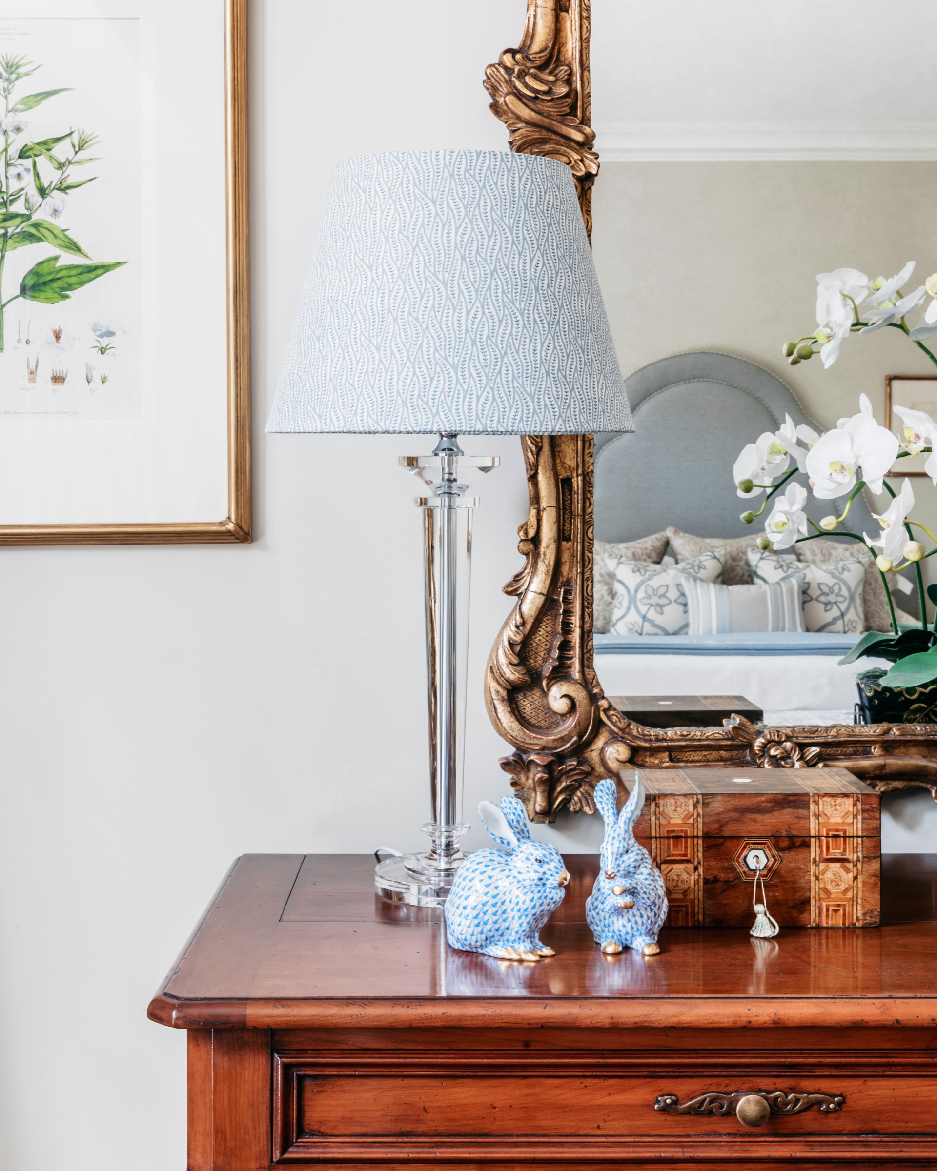 A bedroom chest with a blue lamp and ceramic decorative rabbits.