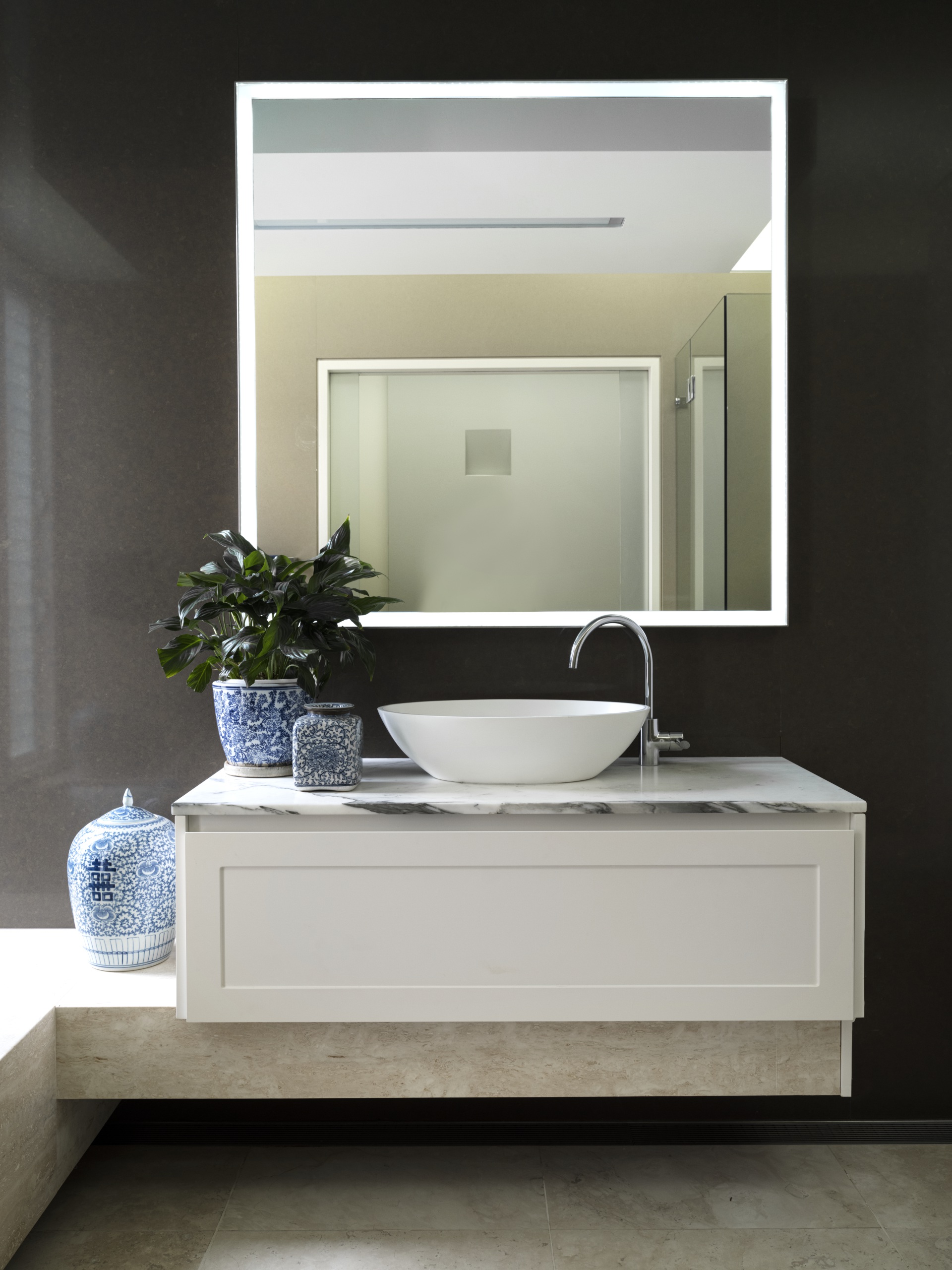 A modern bathroom with a square mirror, marble topped vanity and ginger jars.