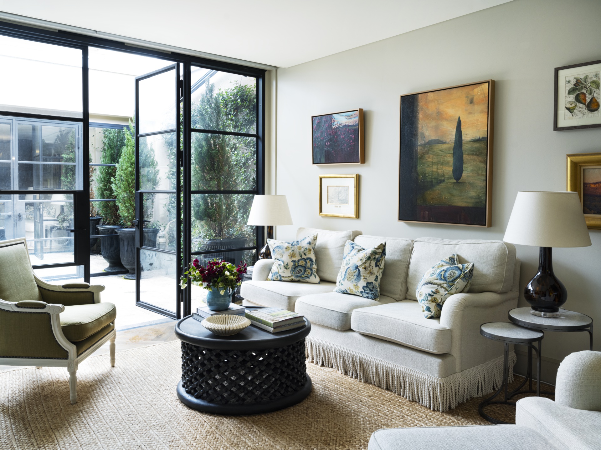 A living room with steel doors, landscape artworks and neutral furniture.