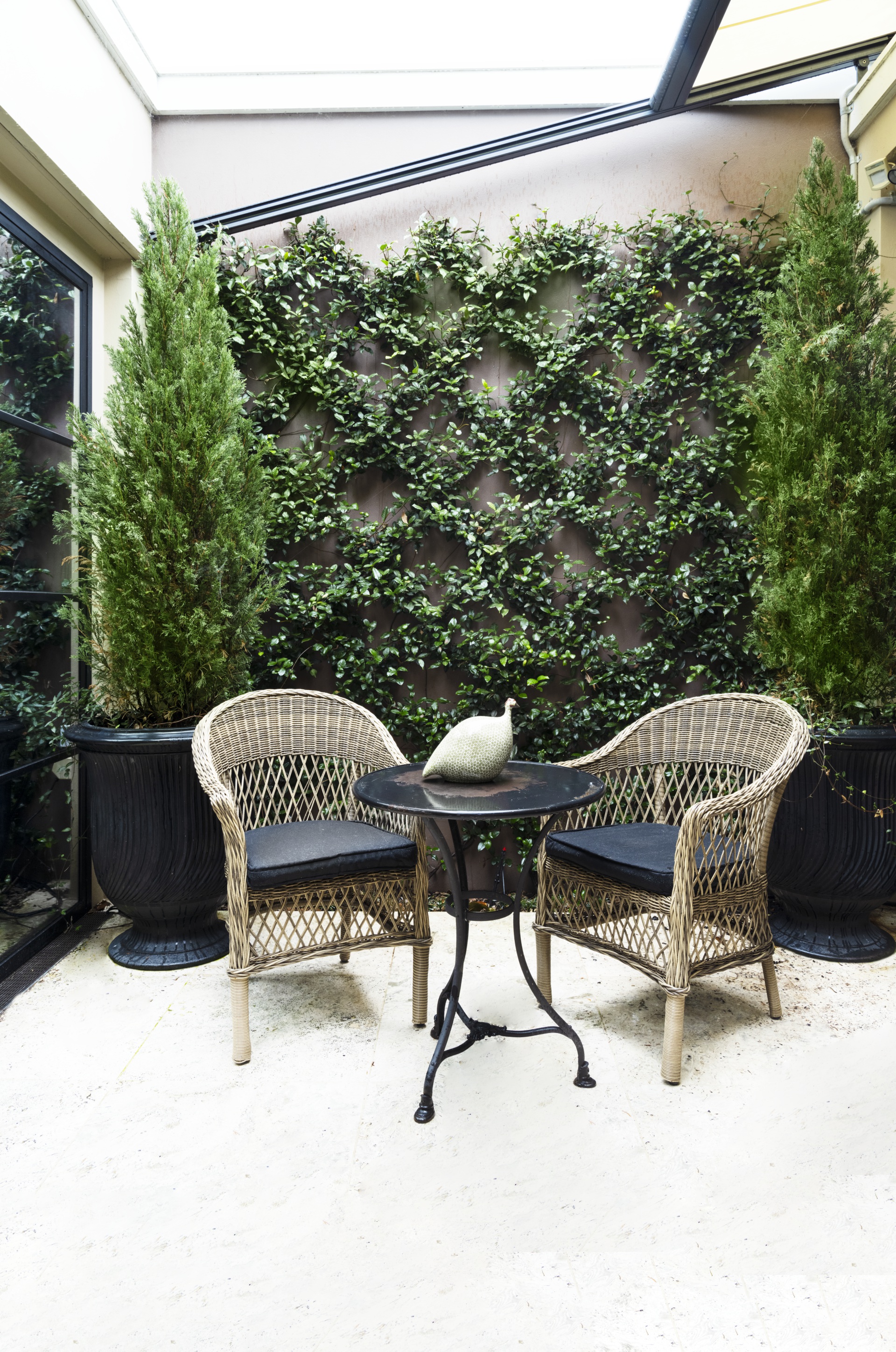 A travertine courtyard with rattan chairs surrounded by greenery.