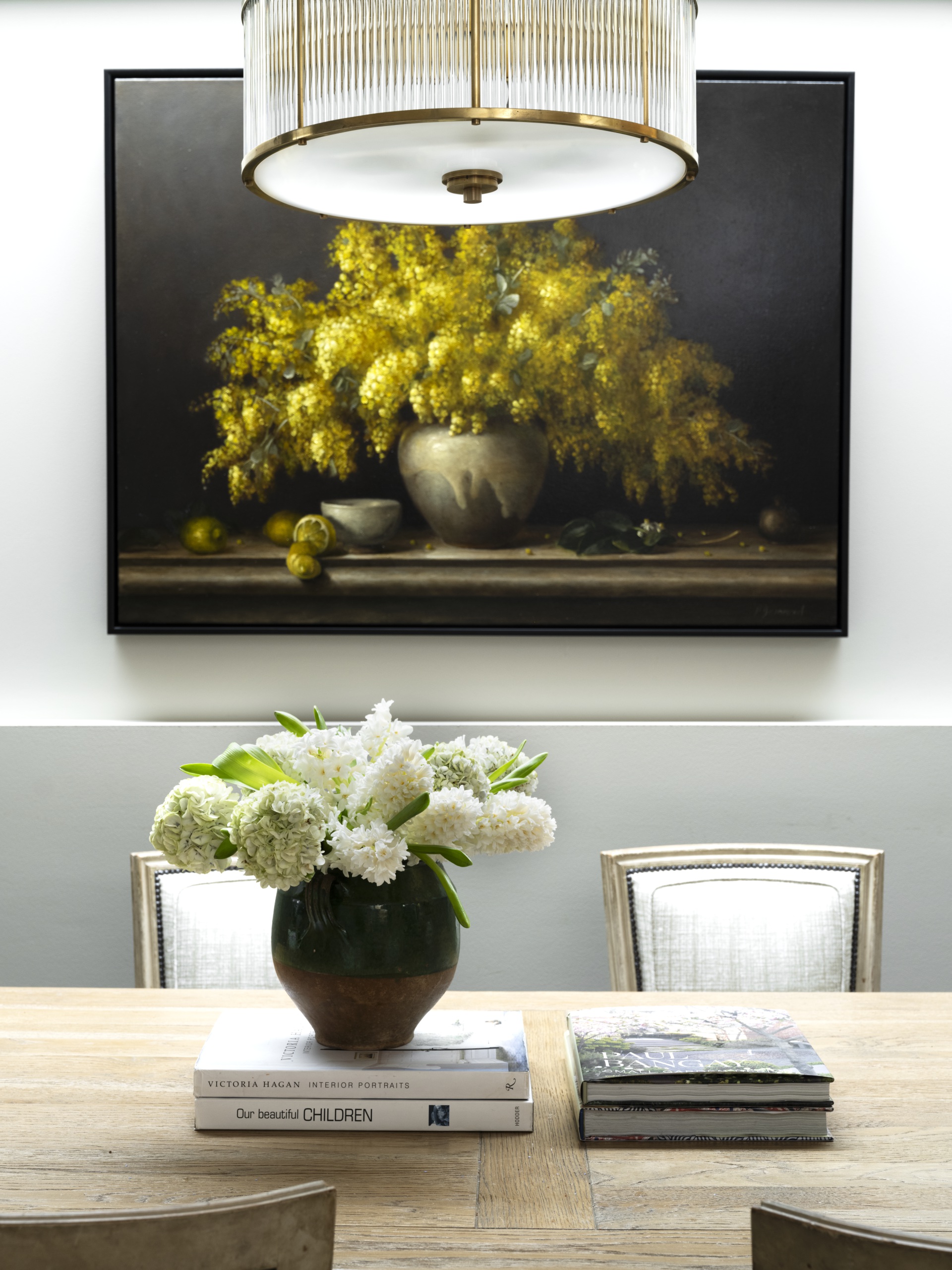 A vase of white flowers on the dining table in front of a dark floral artwork.