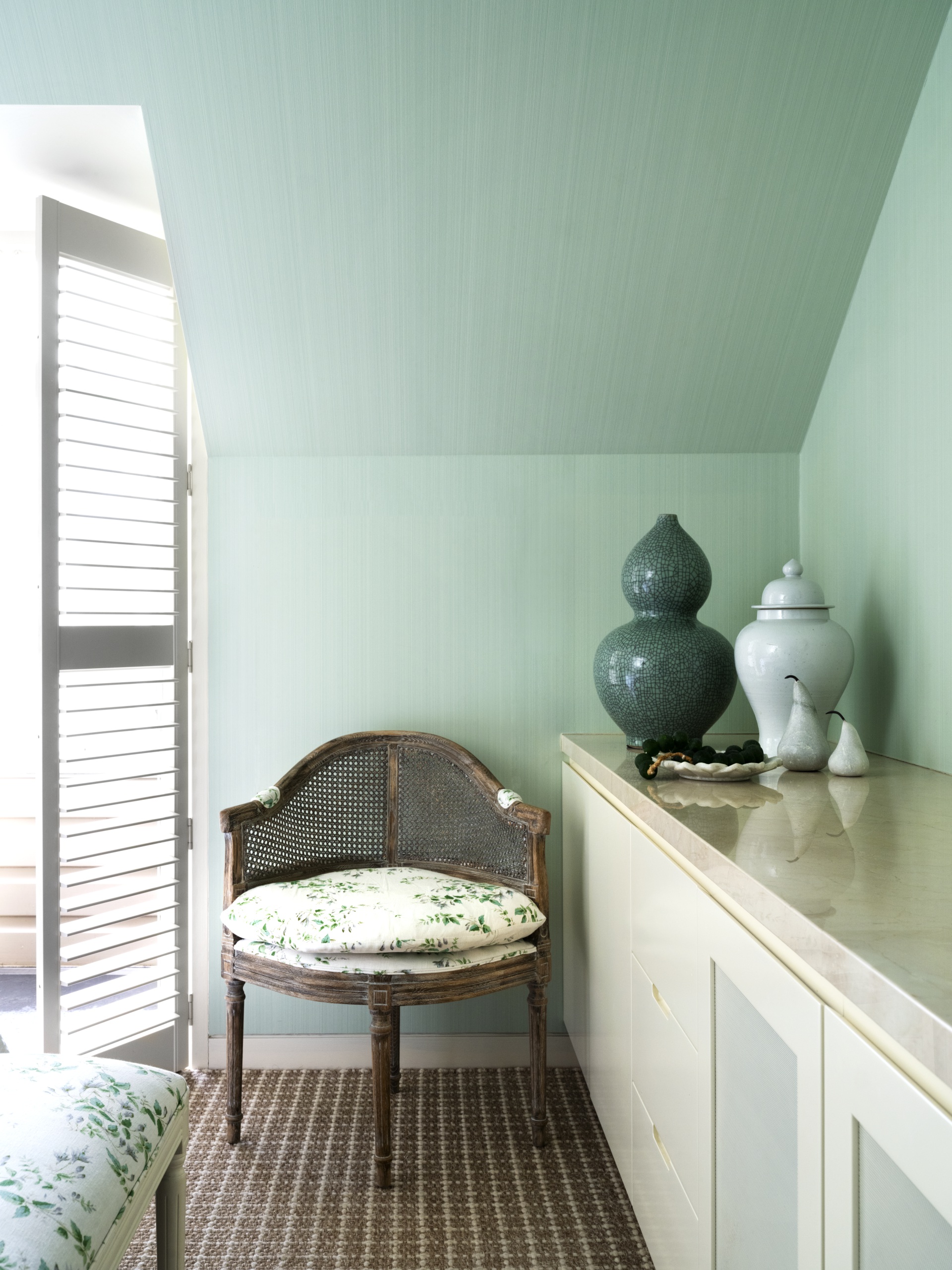 A vintage bedroom chair beside a console and ceramic jars.