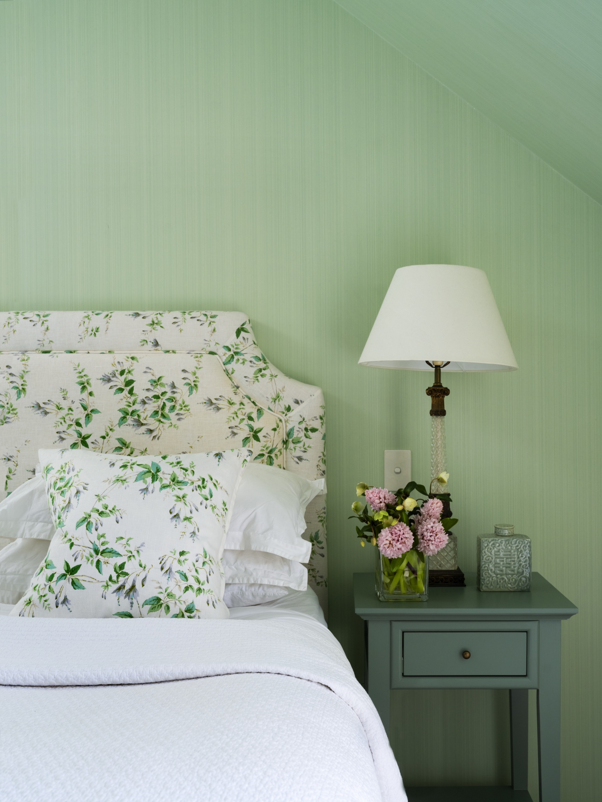 A pastel green main bedroom with a floral bedhead and vintage furniture.