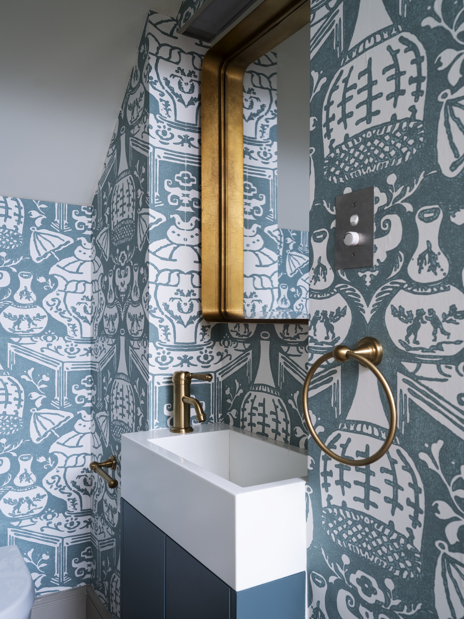 A quaint powder room with decorative blue vase wallpaper.