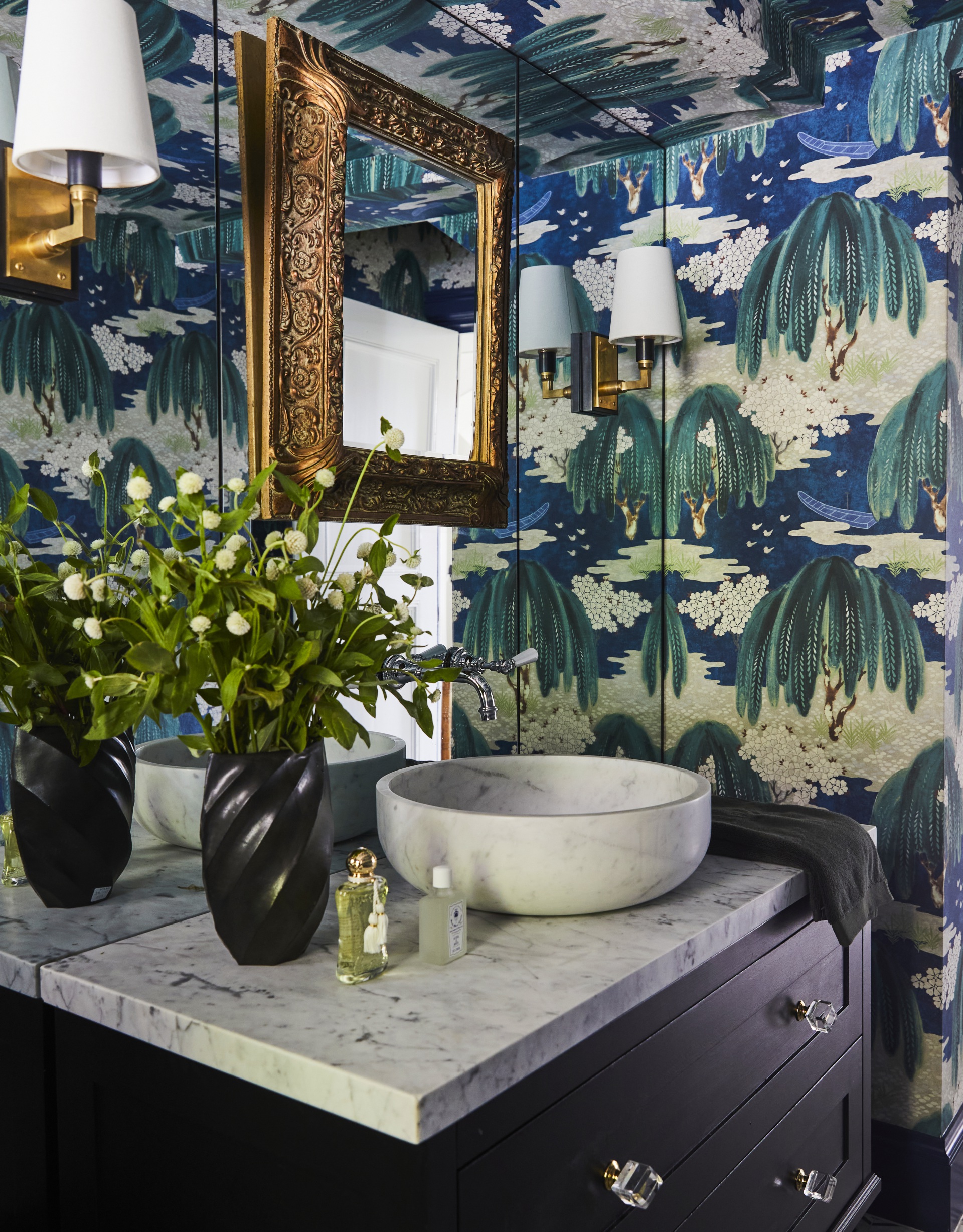 A powder room with blue and green botanical wallpaper and a marble vanity.