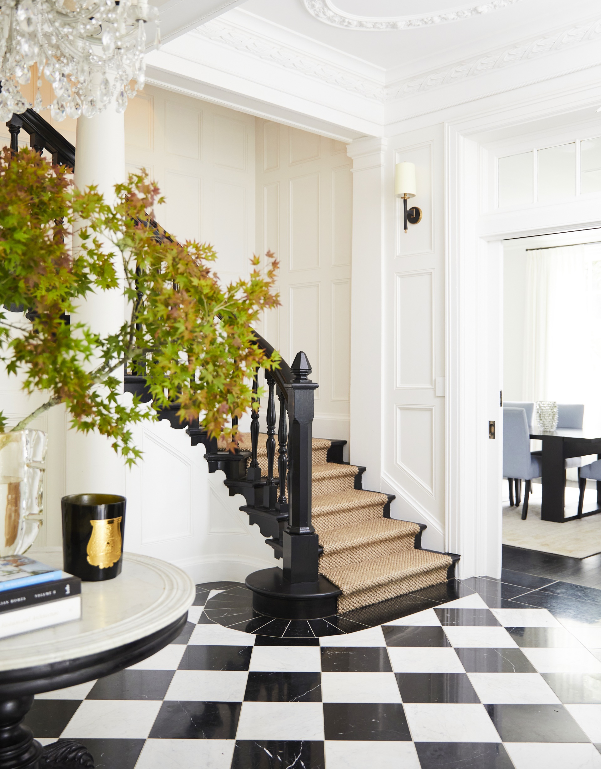 An entry foyer with a black and white staircase, chandelier and checked floor.