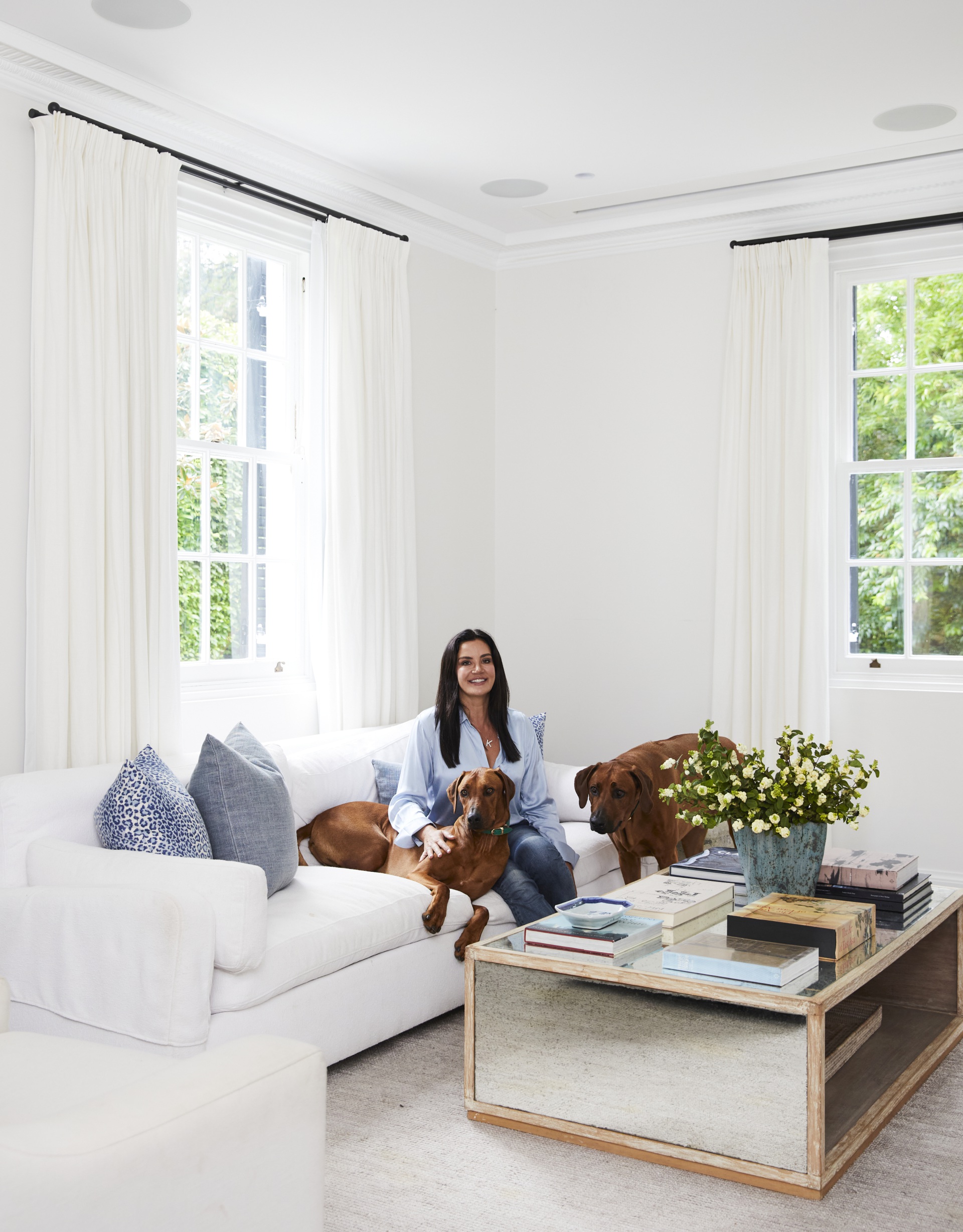 Krissy Marsh and her dog sitting on a sofa in the all-white living room.