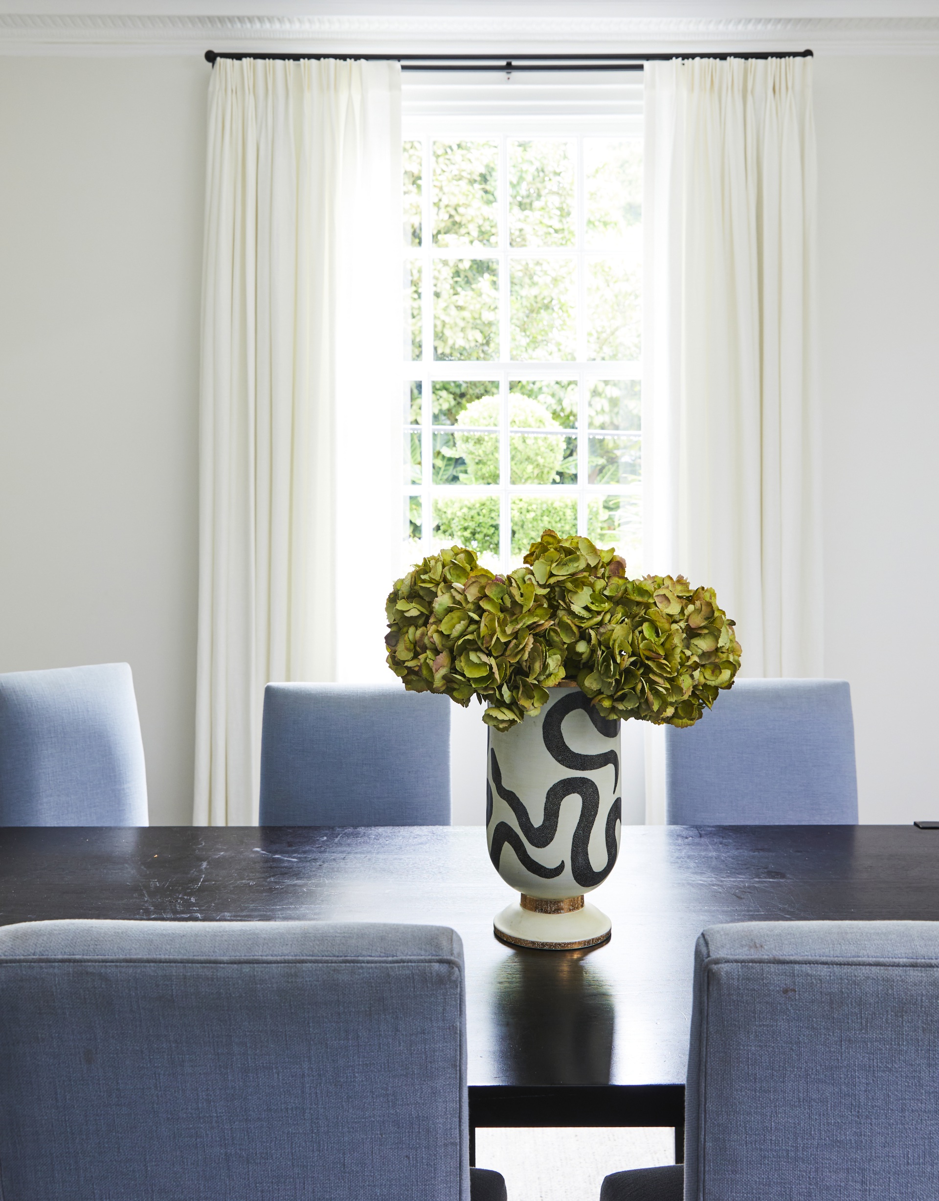An abstract painted vase sitting on a timber dining table.