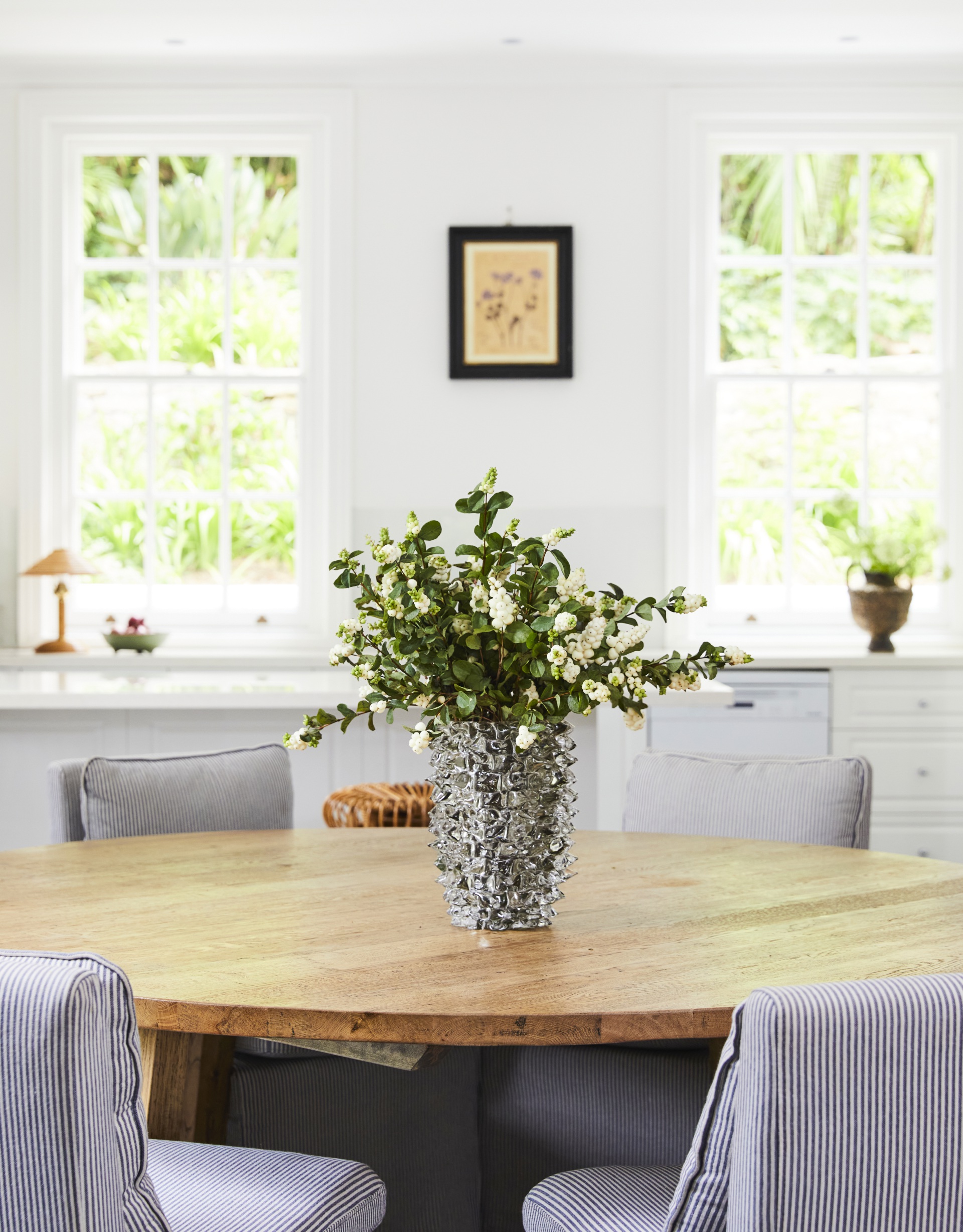A round timber table topped with a vase of white flowers.