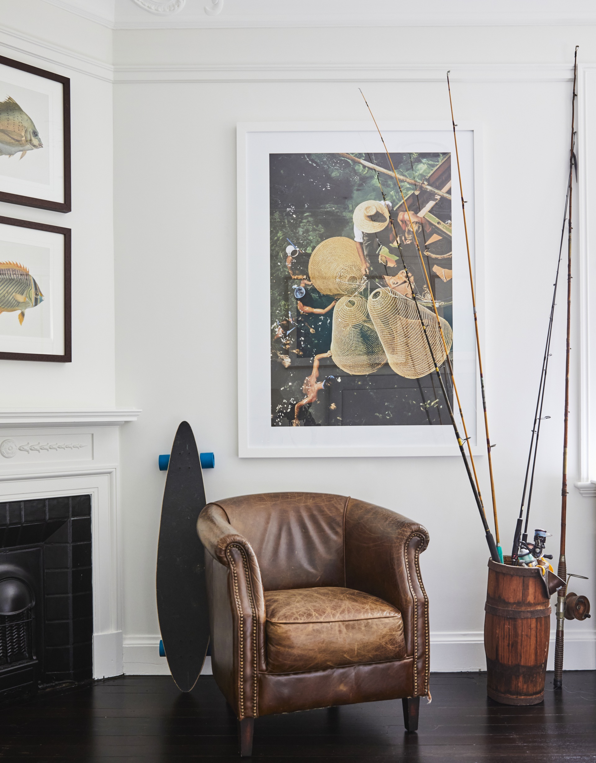 A vintage leather chair beside fishing rods and a classic white fireplace.
