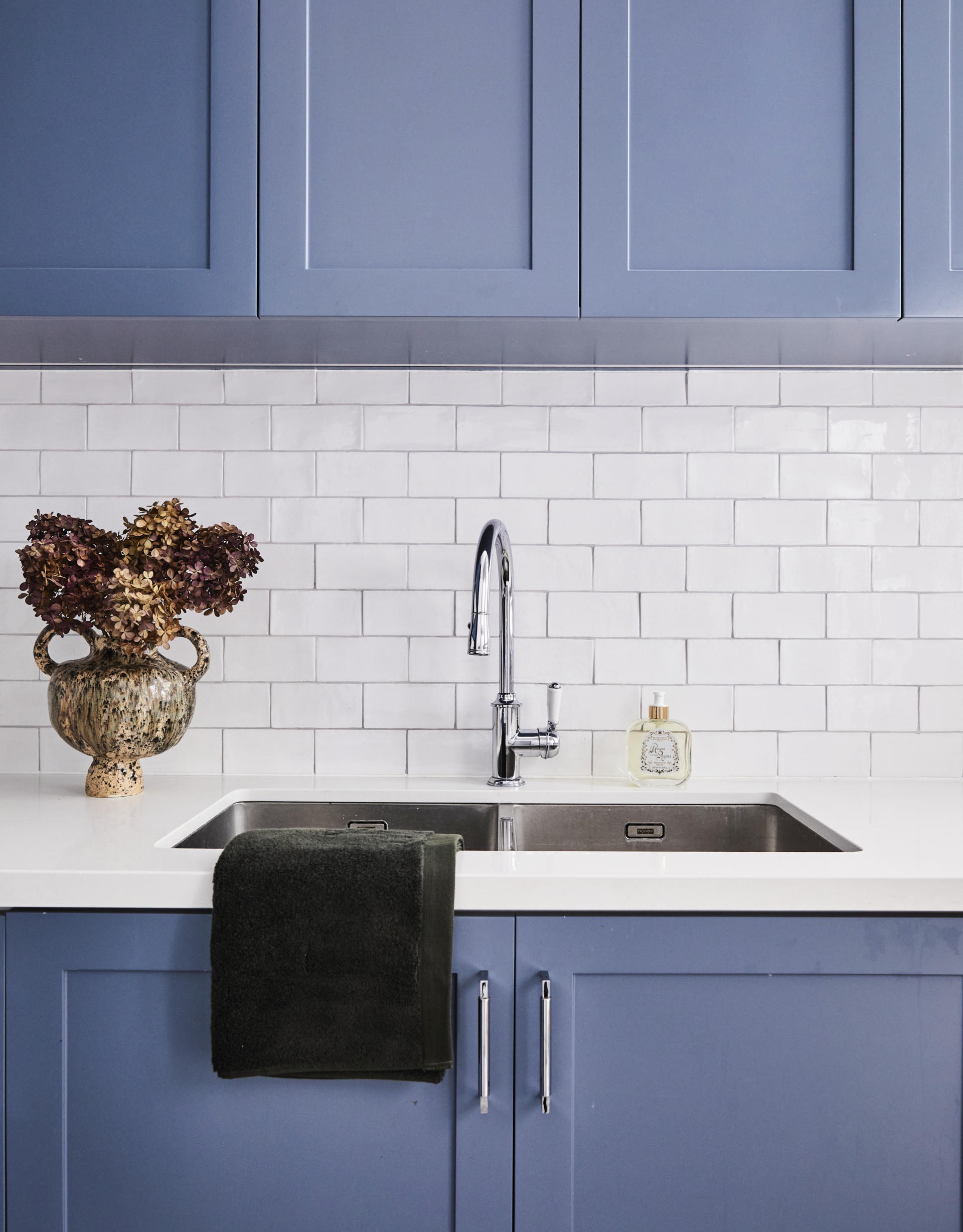 A laundry room with blue shaker-style cabinets and white subway tiles.