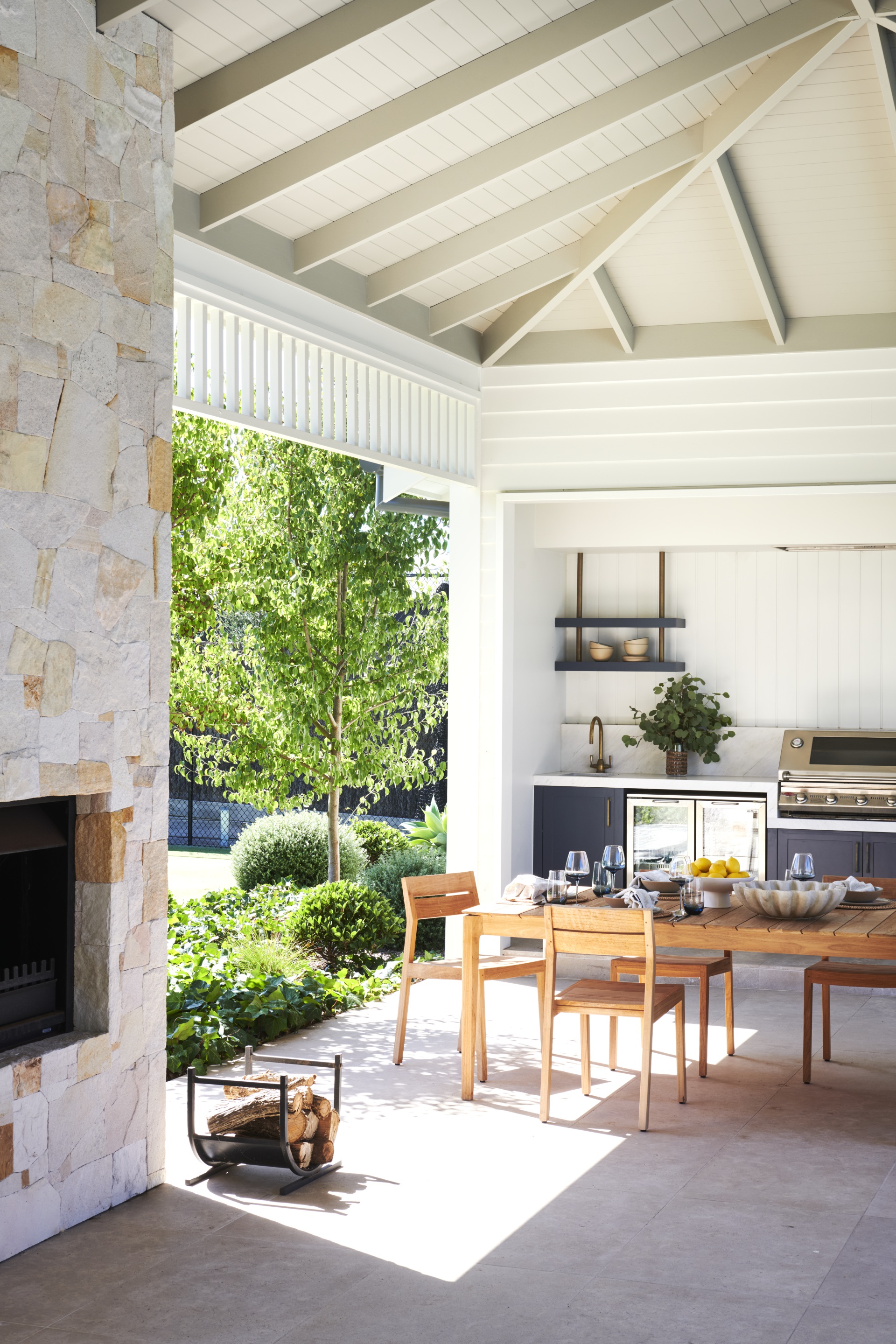 An outdoor alfresco area flanked by a stone fireplace.