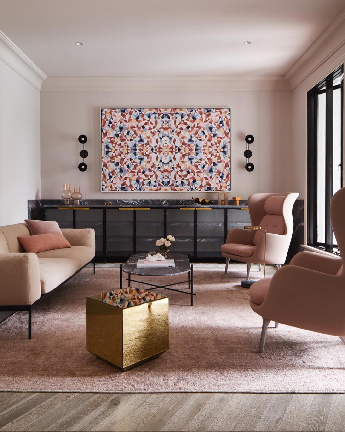 A pink sitting room with two pink armchairs, one pink sofa and a geometric artwork on the wall.
