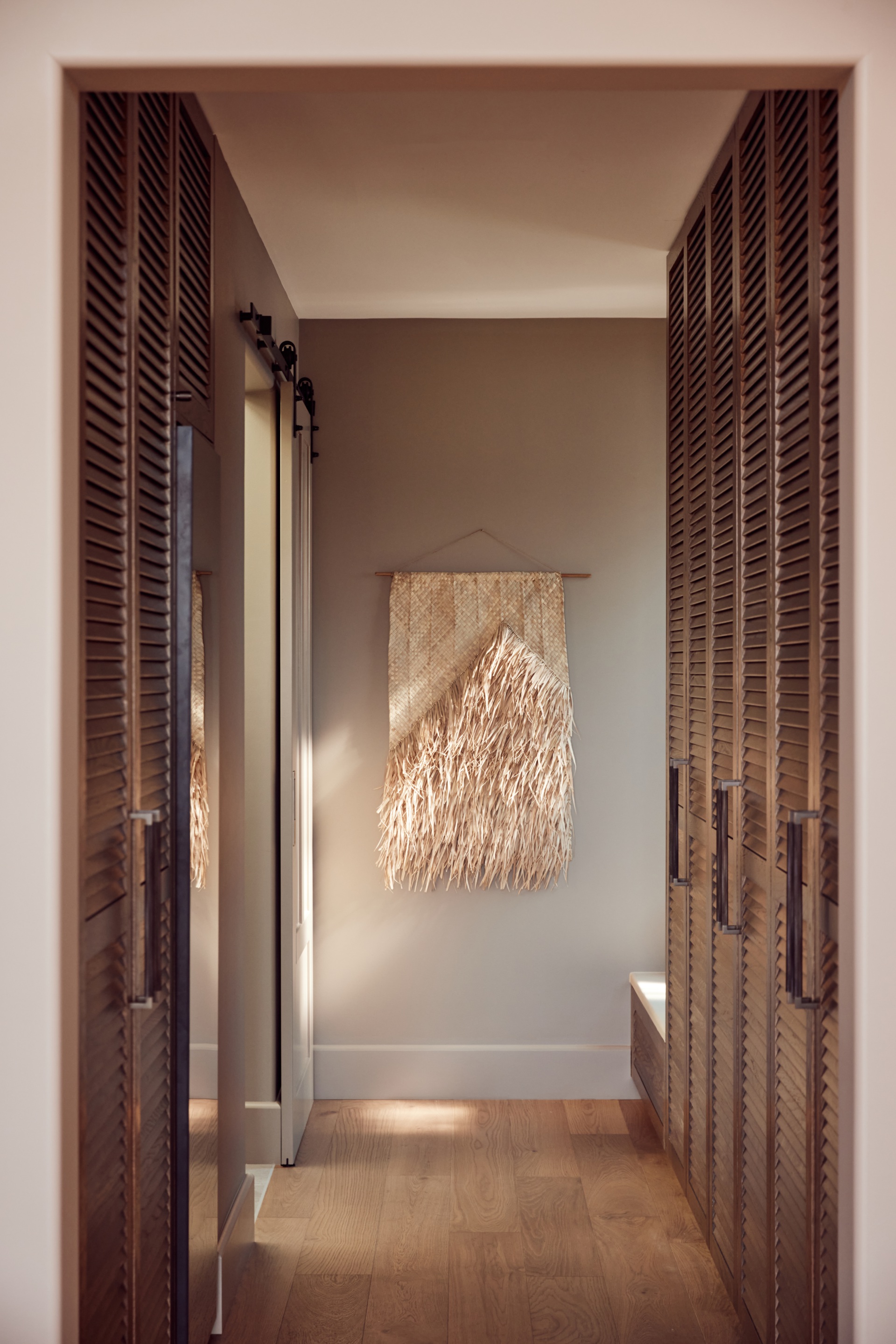 A walk-in-robe with dark cabinetry and a textured woven artwork.