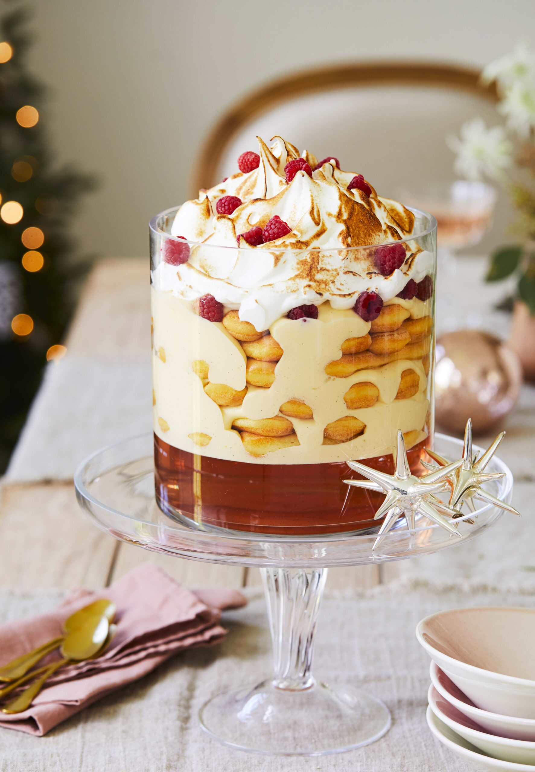 Rose and zabaglione trifle recipe served in a tall glass cylinder atop a glass cake stand with Christmas decorations