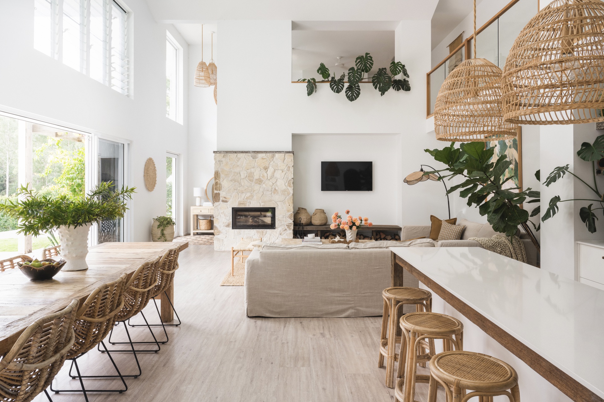 An open plan kitchen, dining and living area with mediterranean coastal style interiors, including white, reclaimed timber and a stone wall.