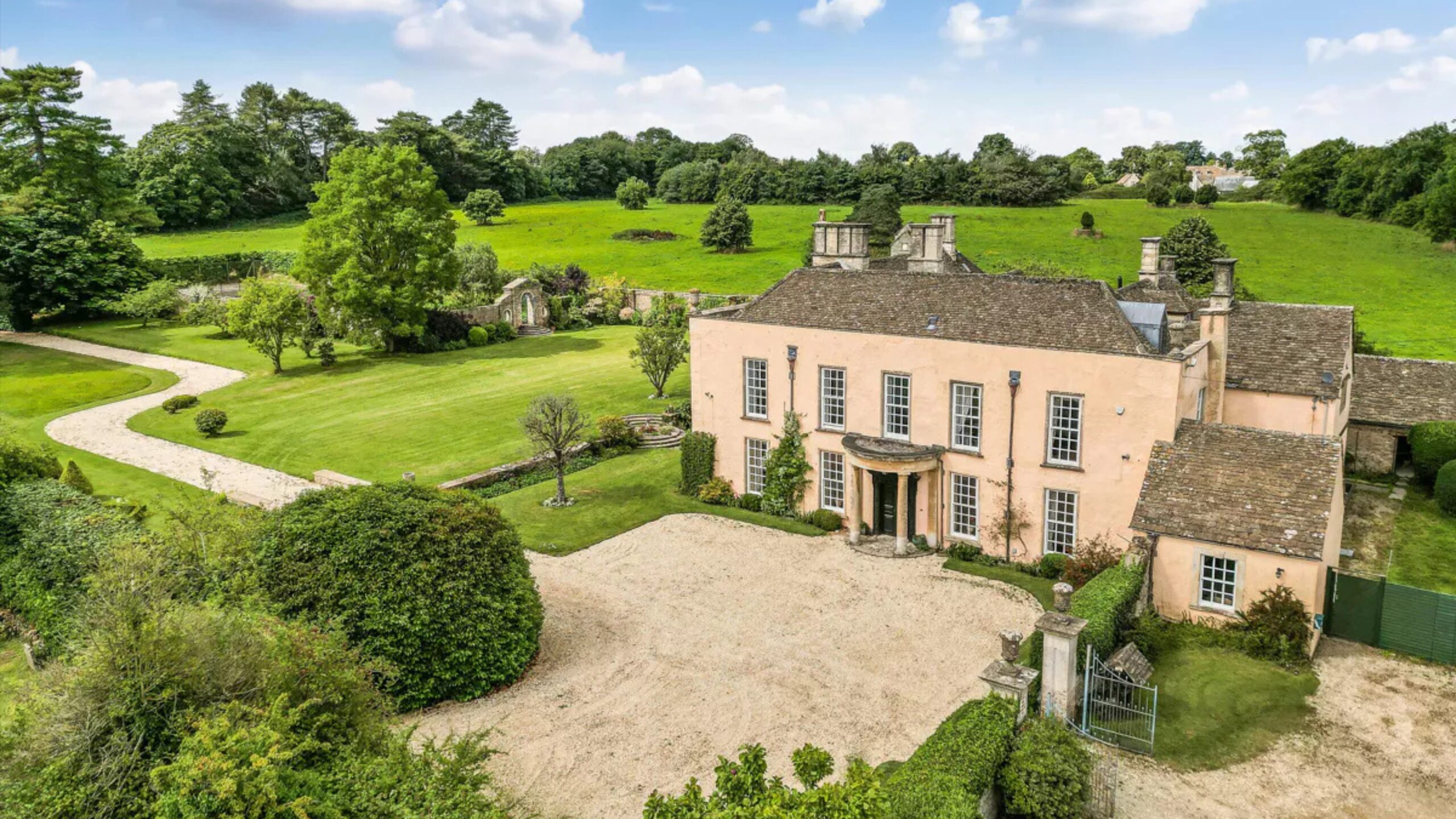 A grand stone manor house, built in 16th Century style with a Queen Anne front pillared portico. Grounds surround the home with trees, hedges, bushes and lush grass. This house was the filming location of the Bennet family house in the BBC adaptation of Jane Austen's Pride and Prejudice.