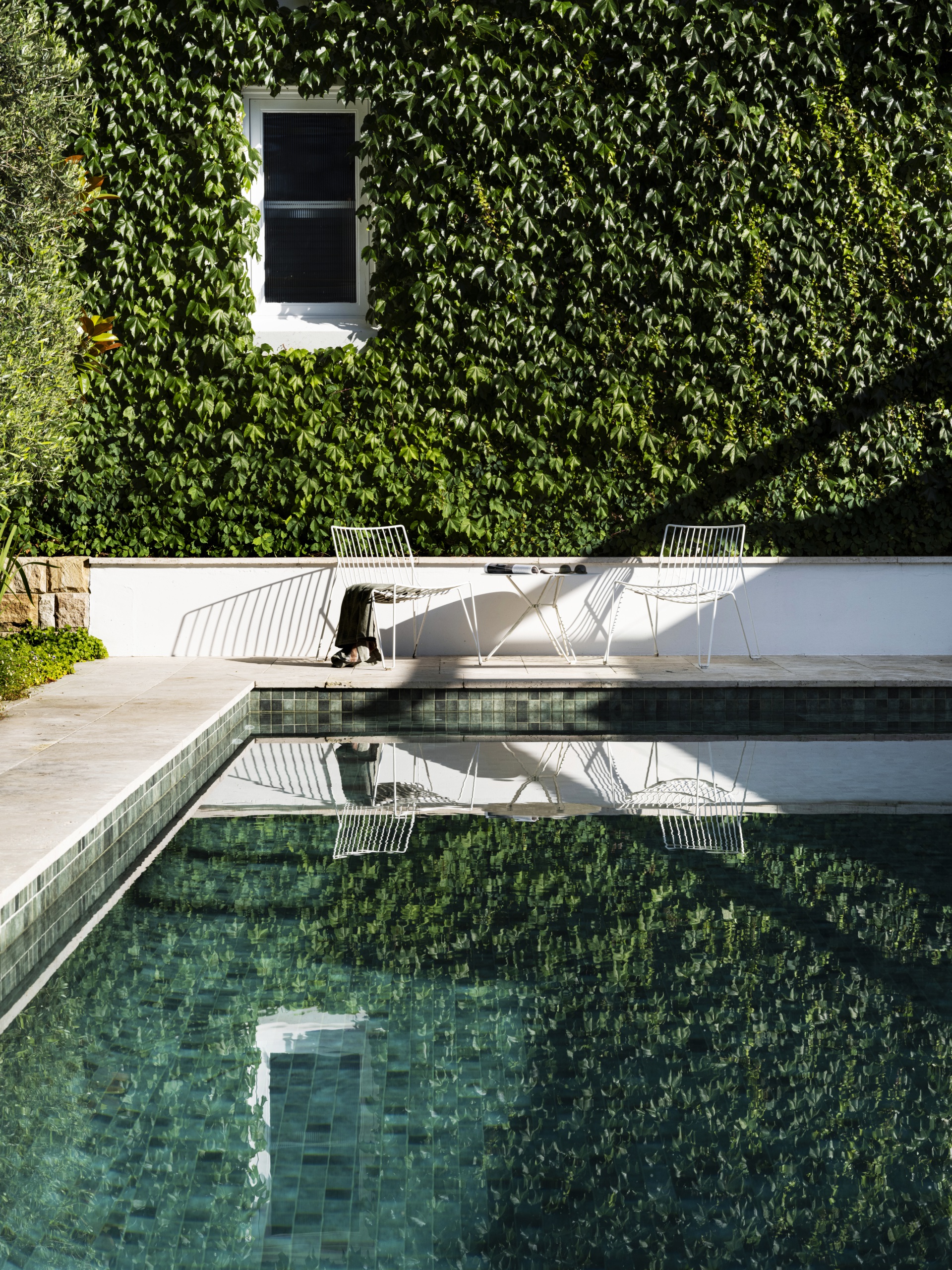 A rectangular swimming pool, surrounded by large stone pavers with a wall covered in Boston ivy in the background.