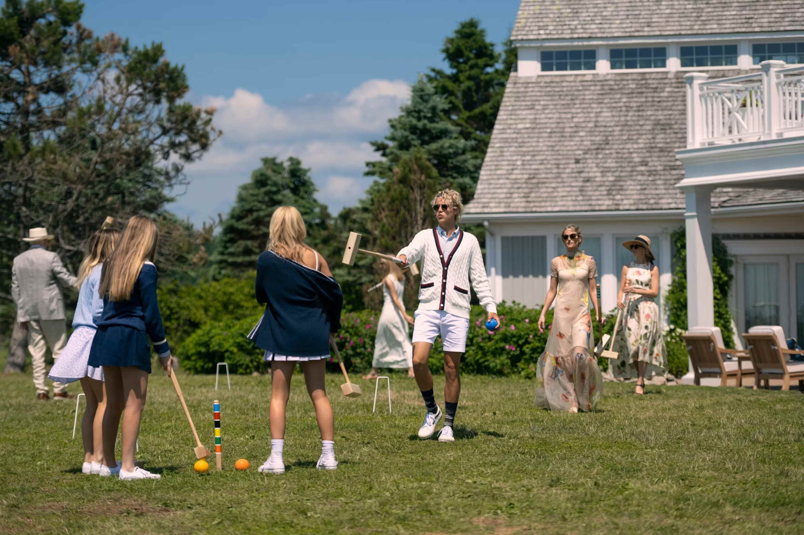 Wealthy family in We Were Liars TV series playing croquet on lawn outside Marthas Vineyard style white house with shingles. 